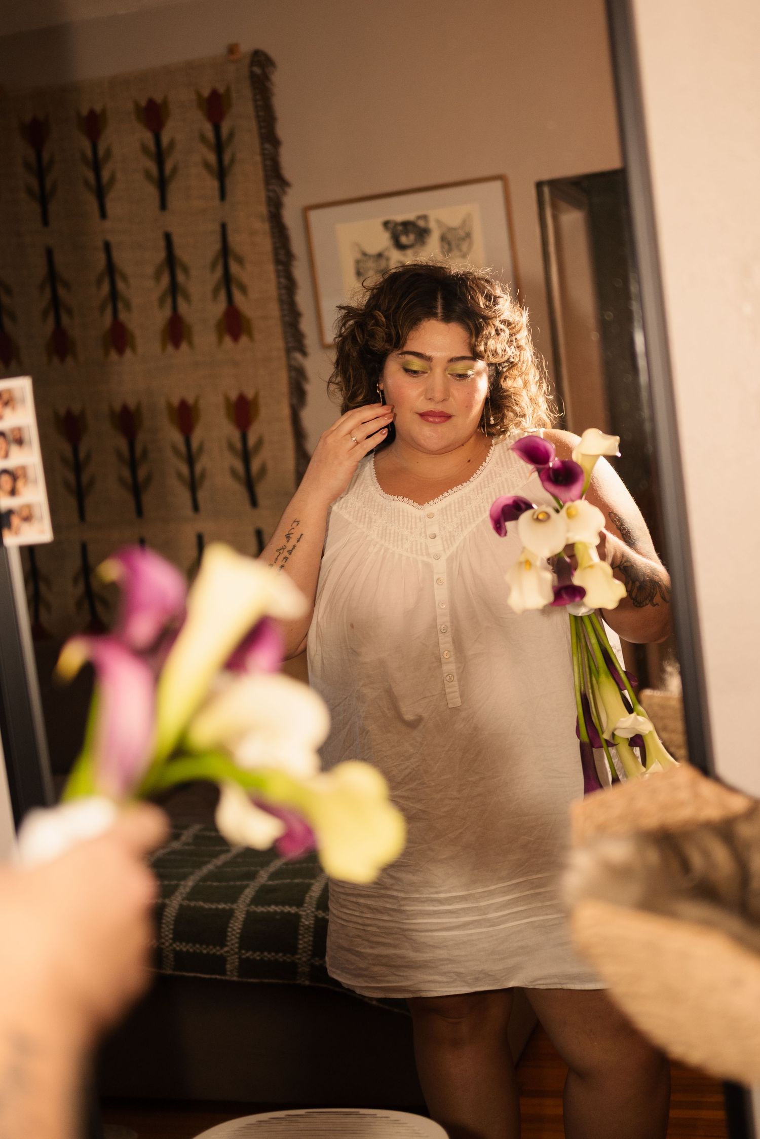 A person in a white sleeveless dress holds a colorful bouquet of flowers in an indoor setting.