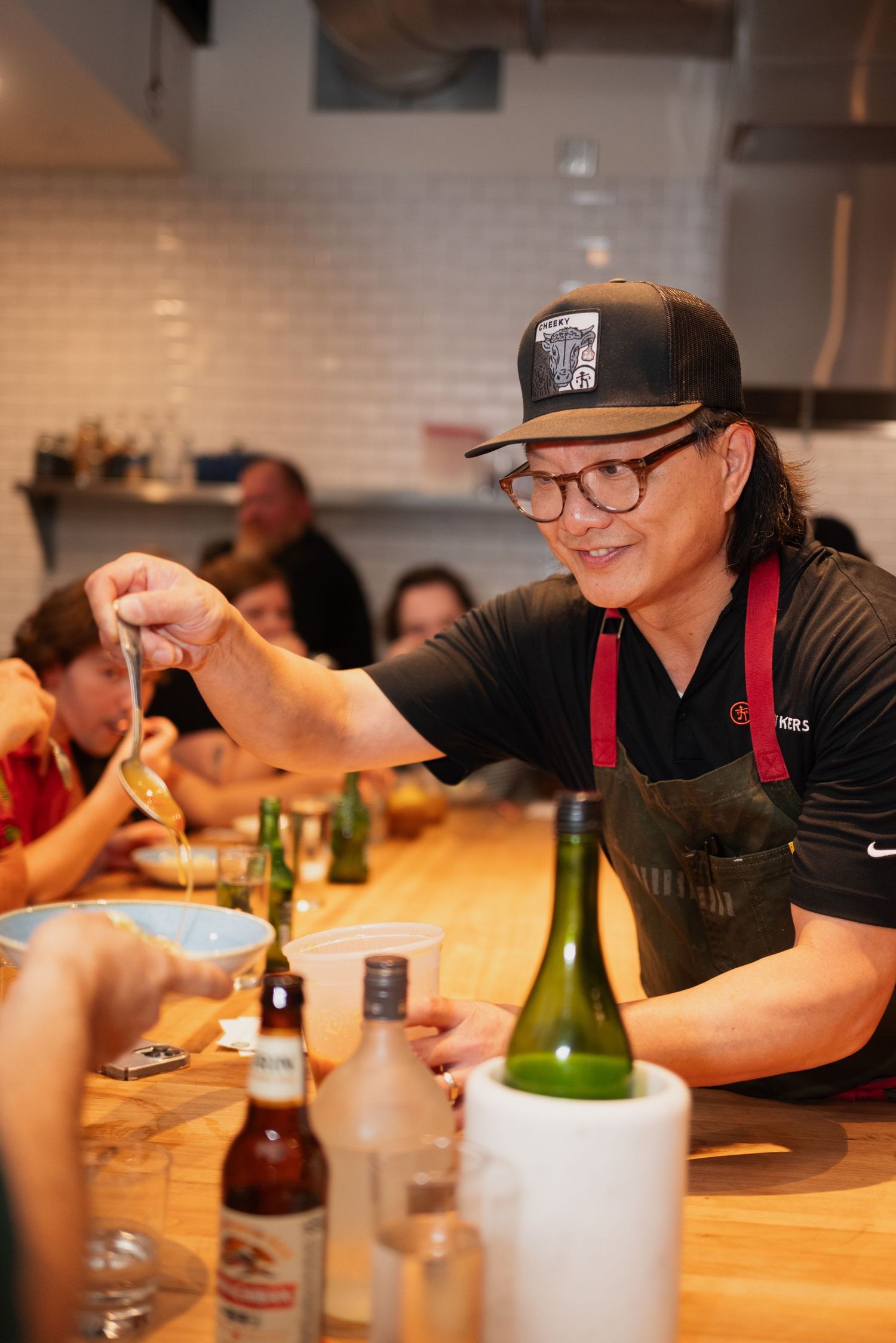 Restaurant staff and patrons gathered around a wooden table with wine bottles.