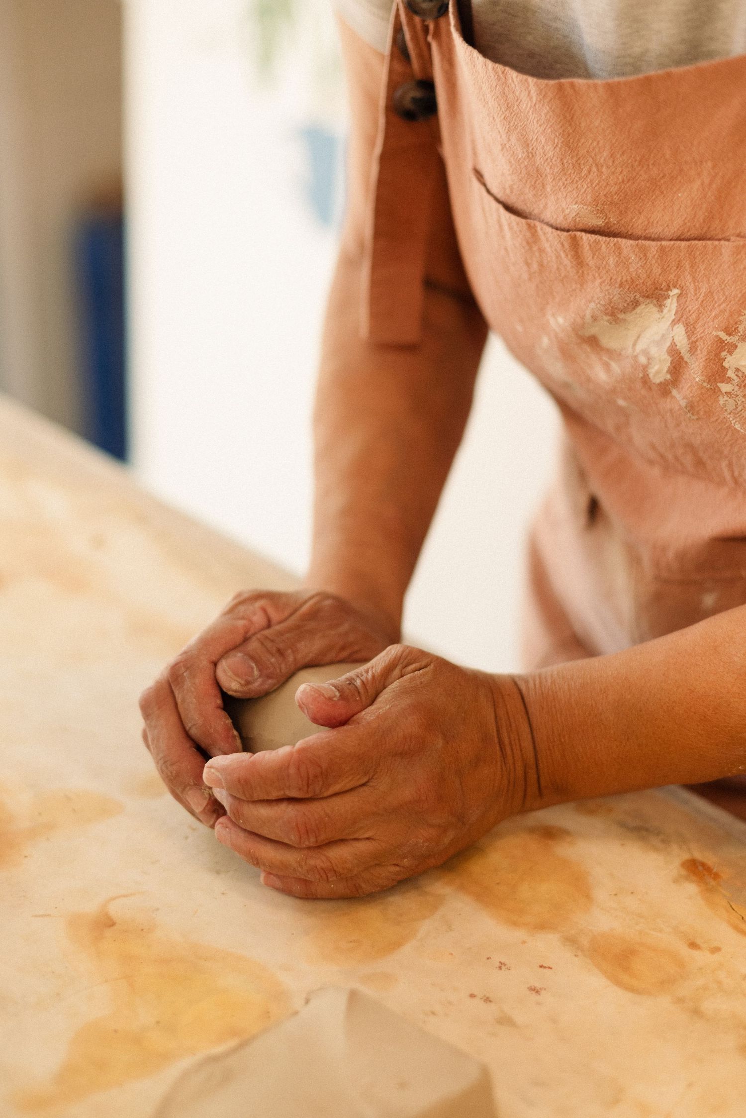Hands kneading dough on a flour-dusted wooden surface while wearing an apron.