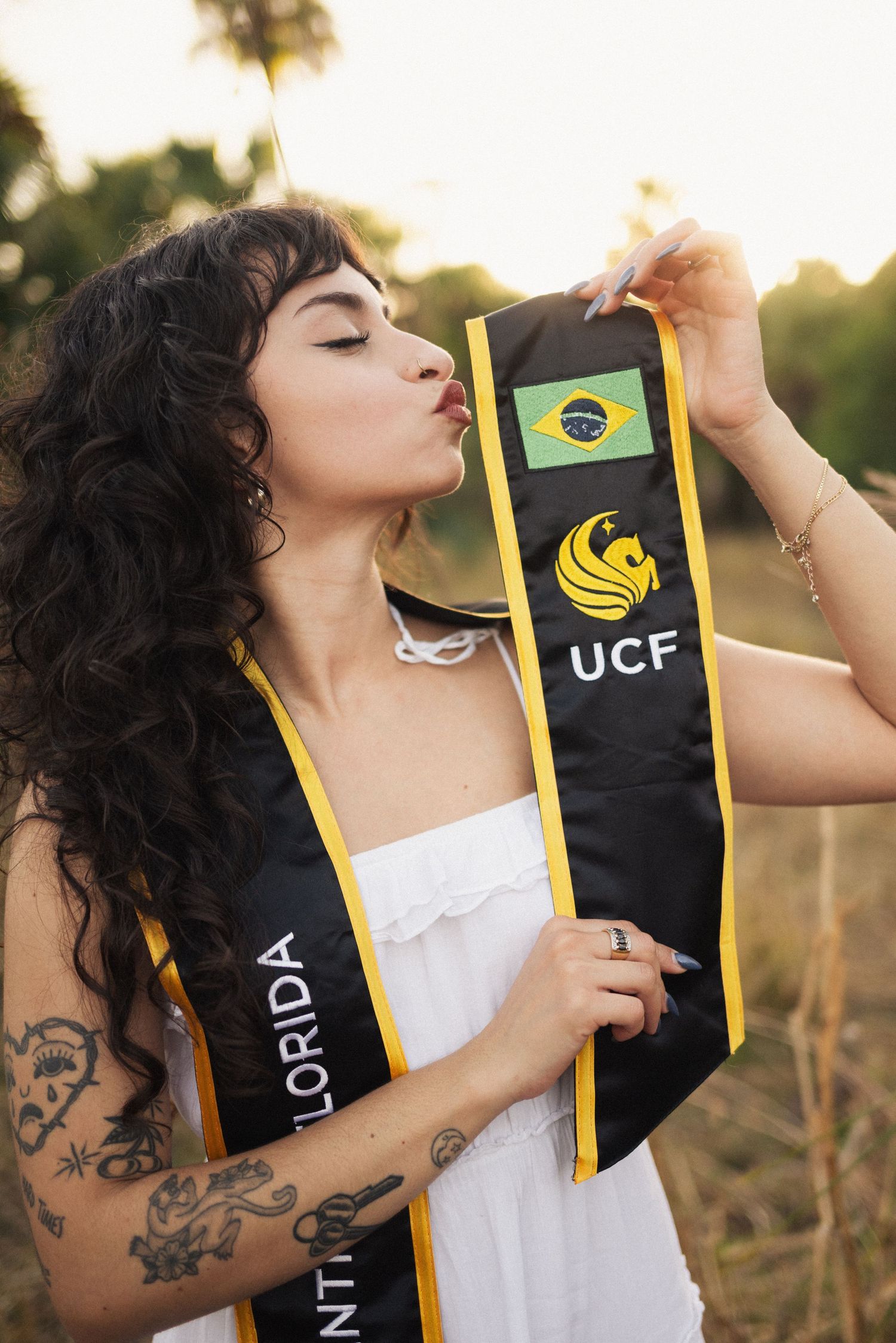 Graduate with curly hair poses with UCF graduation stole during golden hour celebration shoot.