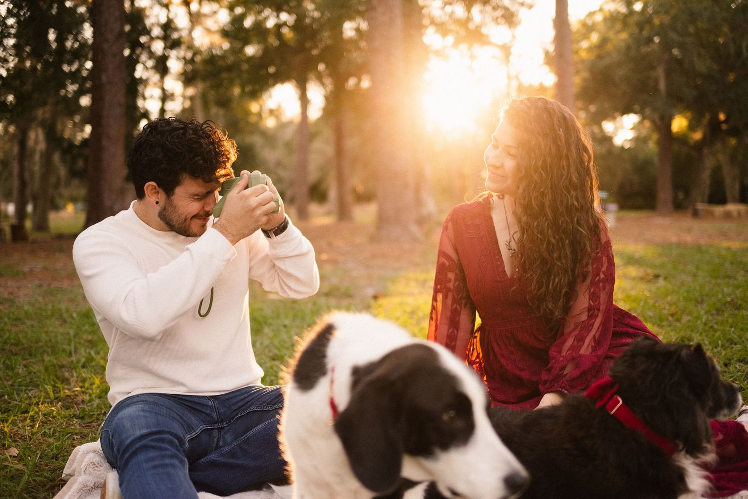 A couple and their dog enjoy a sunset picnic in a grassy park.