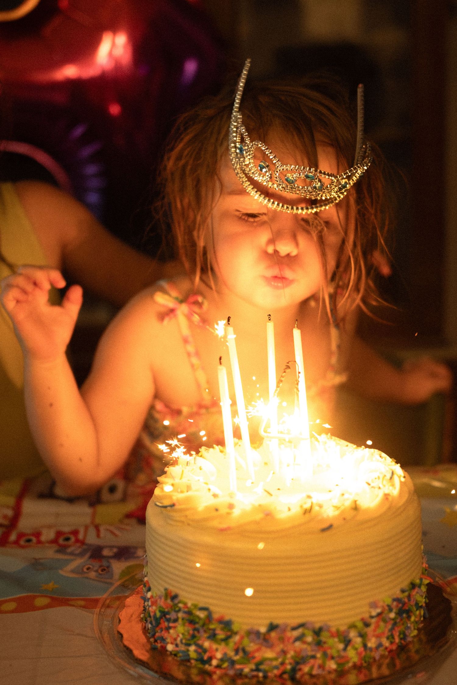 Birthday celebration with lit candles on white frosted cake with colorful decorations.