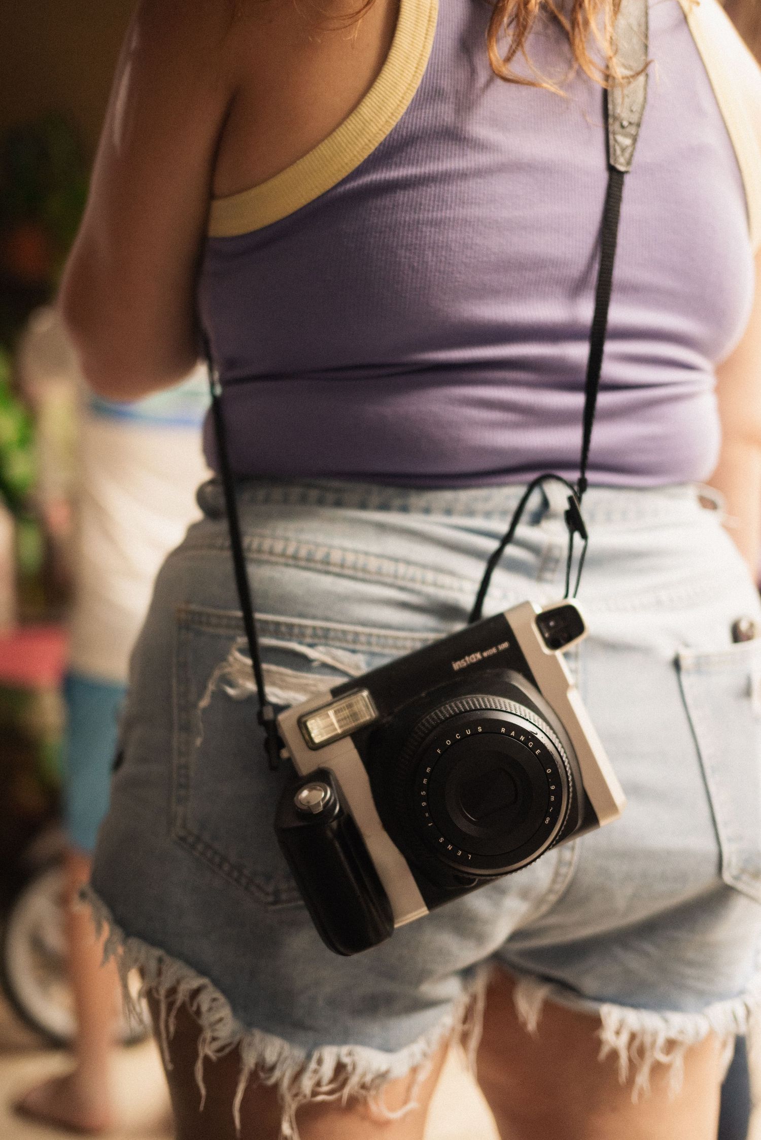 Close-up of a vintage-style camera hanging against light denim shorts.