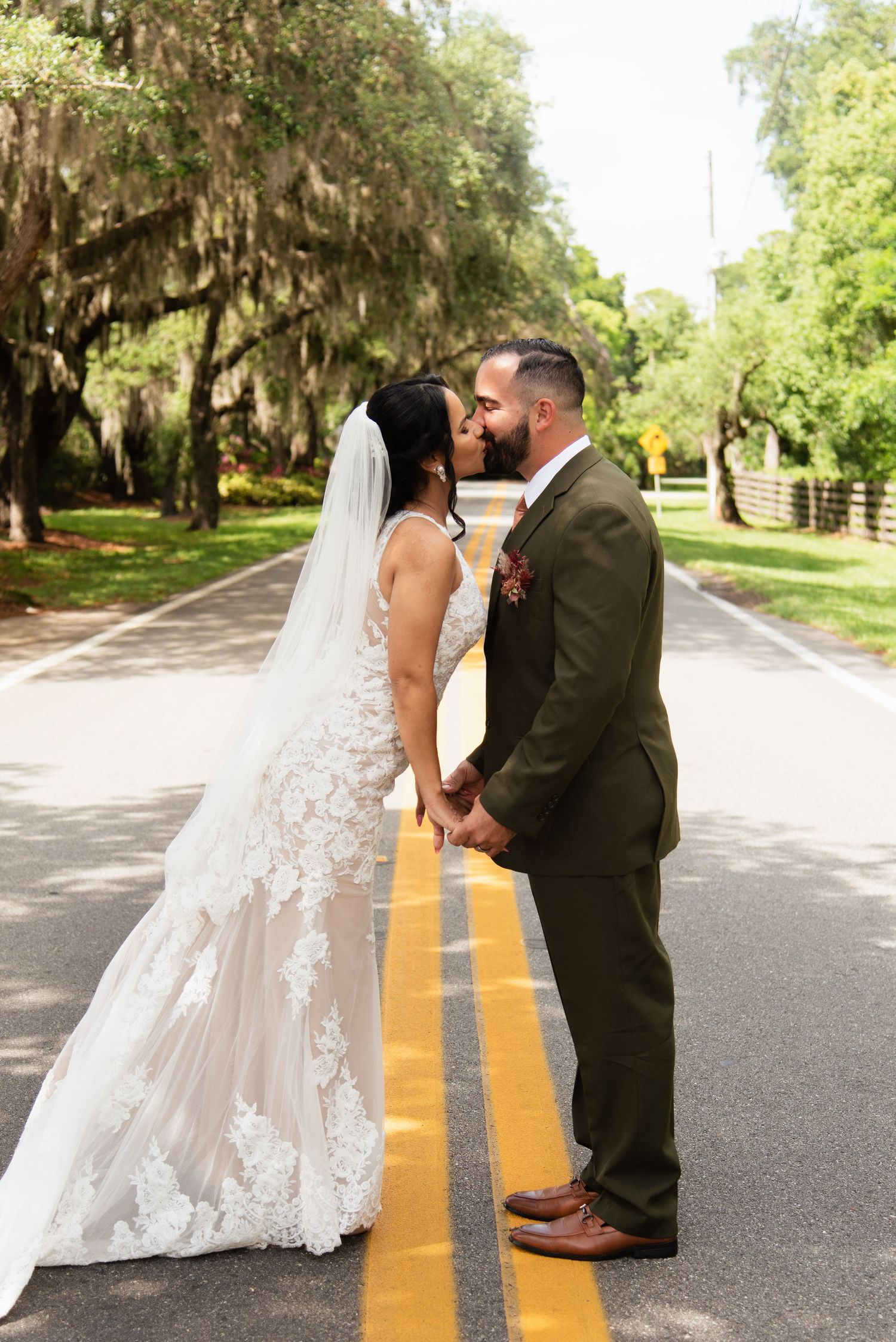 A romantic wedding photo on a tree-lined road with Spanish moss hanging overhead.