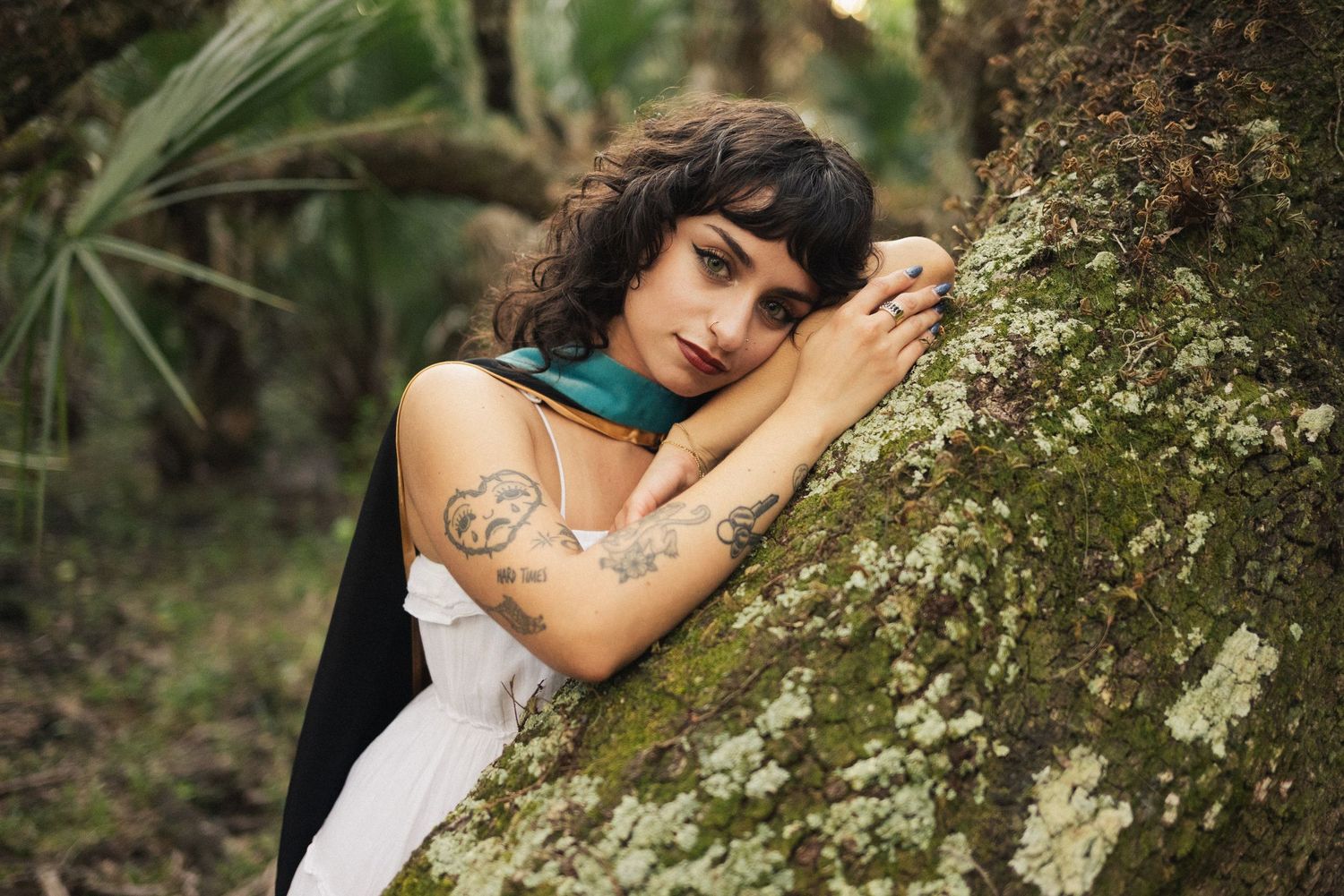 A couple embraces intimately against a mossy tree trunk in a romantic outdoor forest setting.