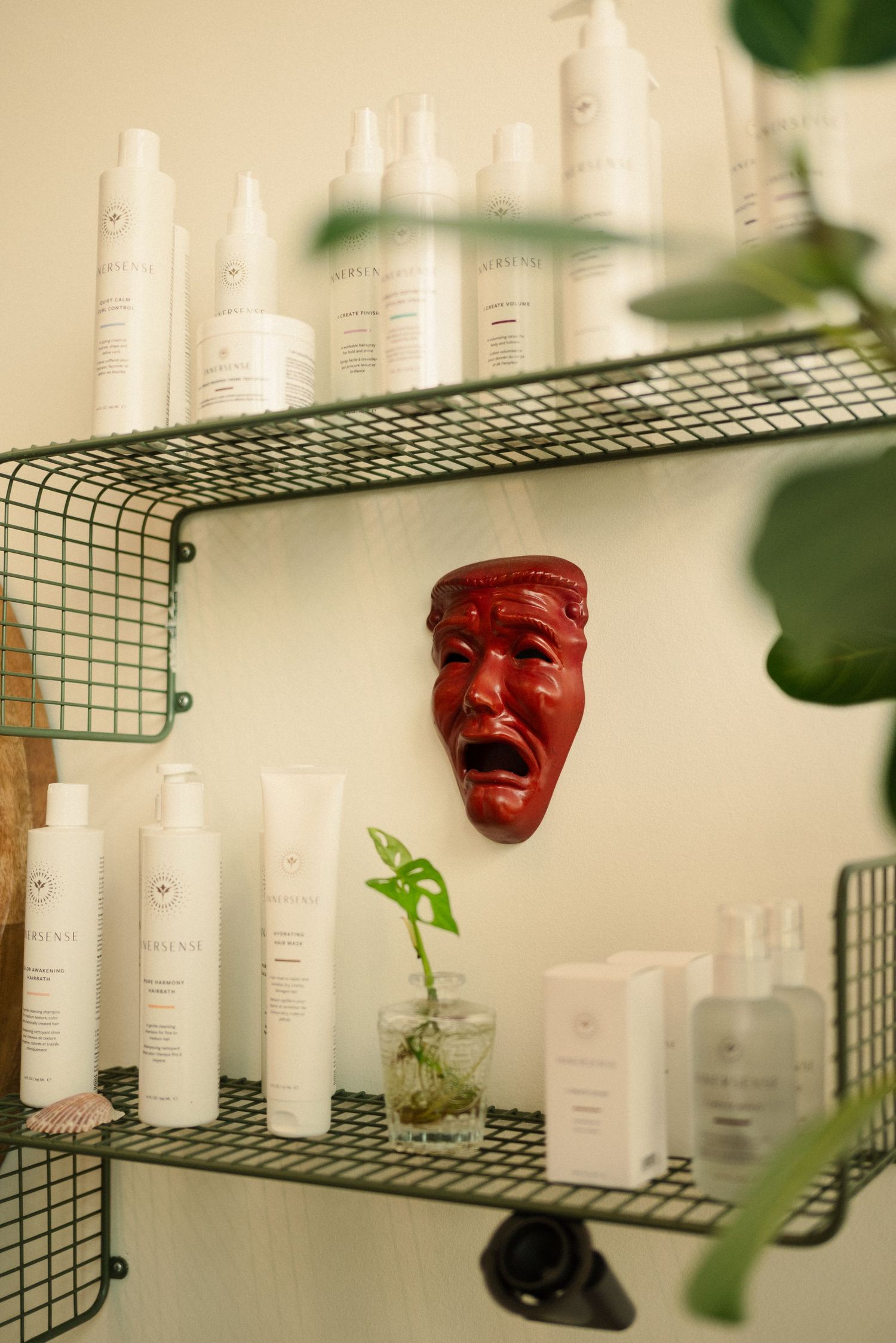 Red theatrical mask mounted on wall between white bottles on wire shelving.