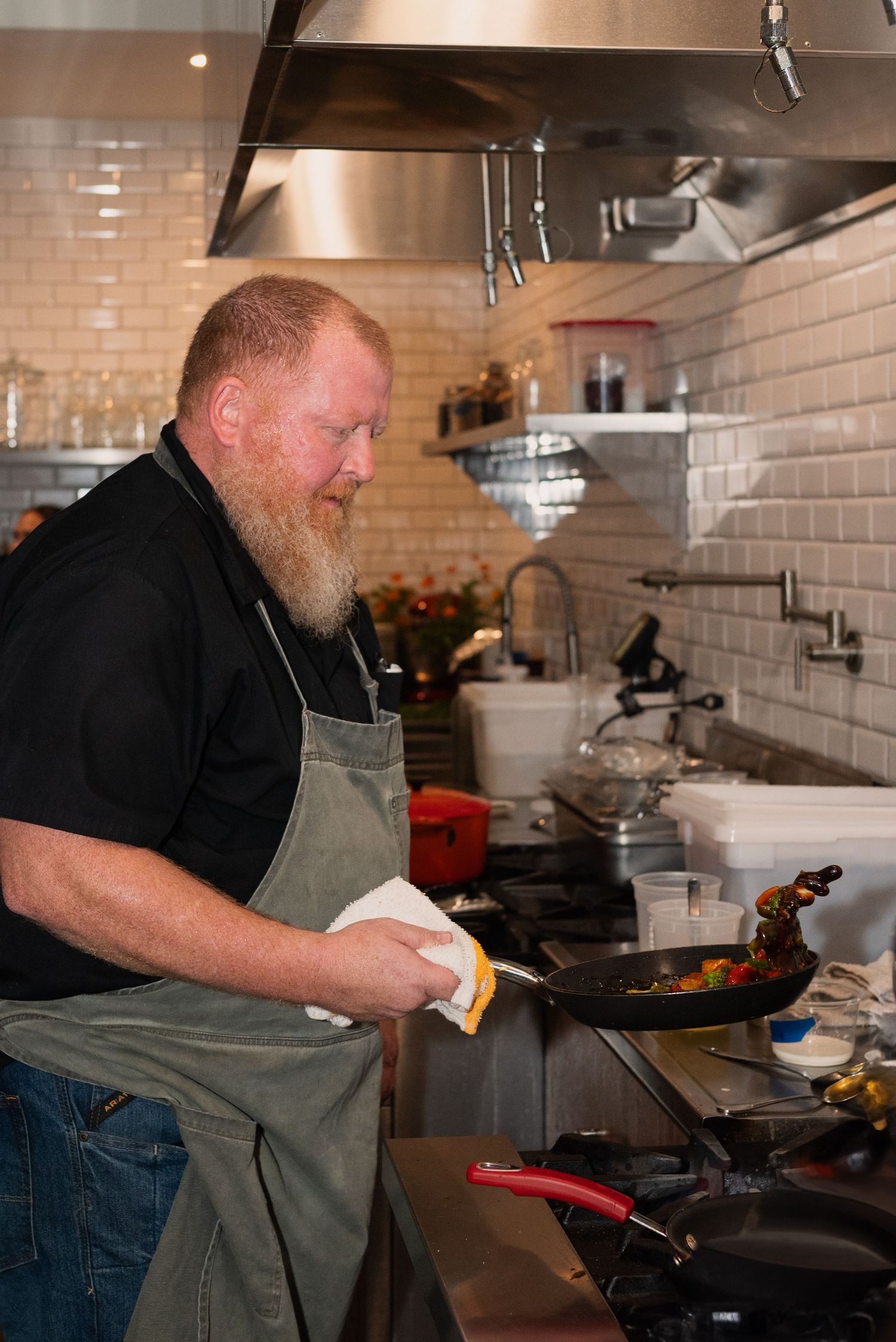 Chef cooking at a professional kitchen station with stainless steel equipment.