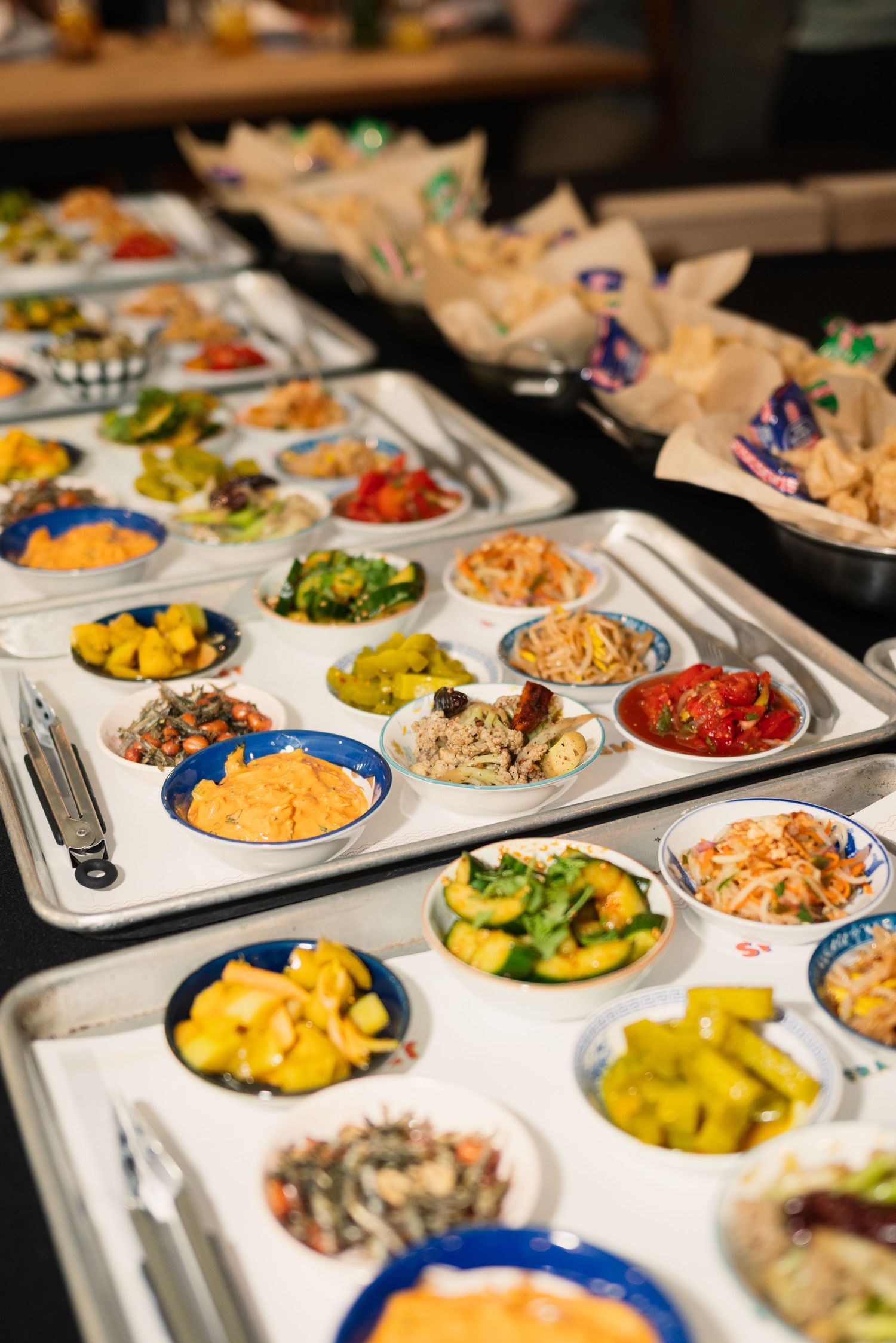 Colorful buffet spread with various dishes served in compartmentalized metal trays.