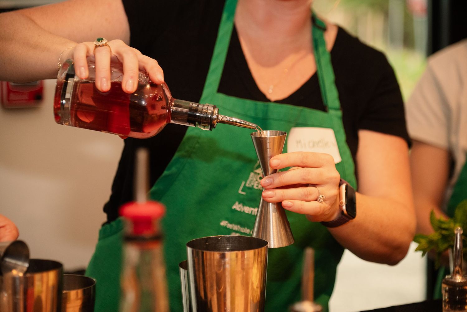 Close-up of hands pouring and mixing cocktail ingredients during a bartending class.