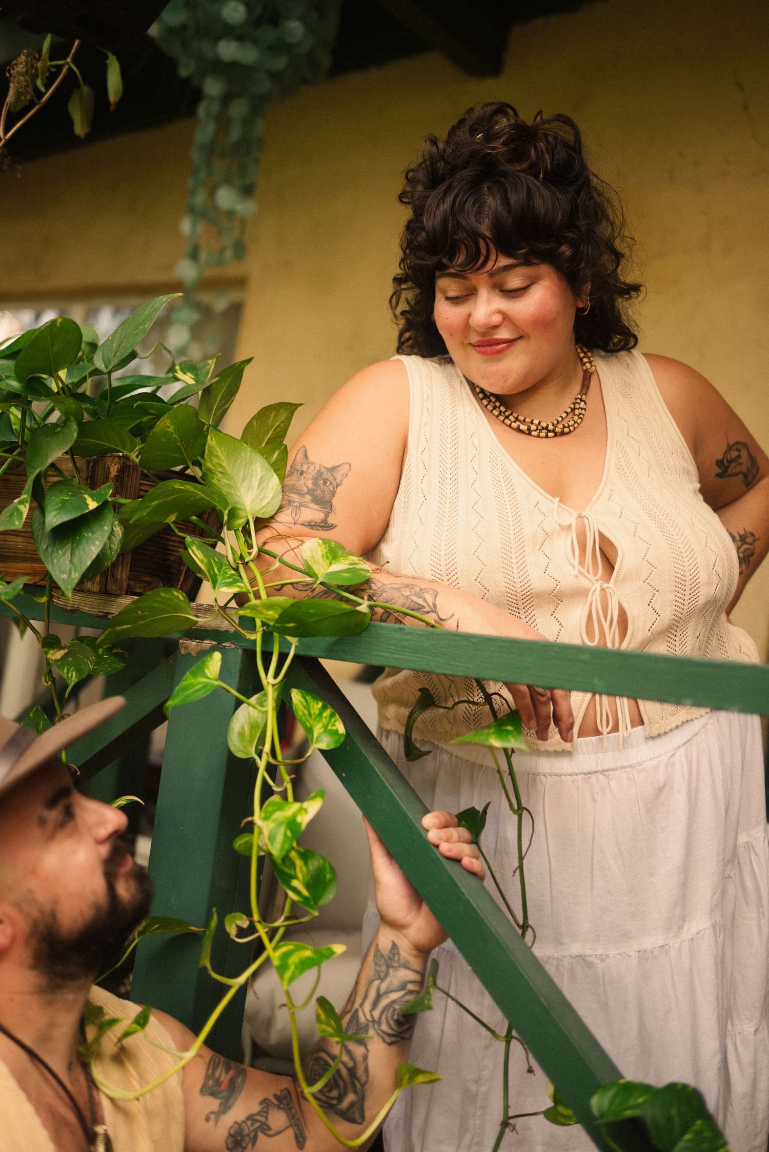 A couple shares a tender moment on a porch with climbing plants and green railings.