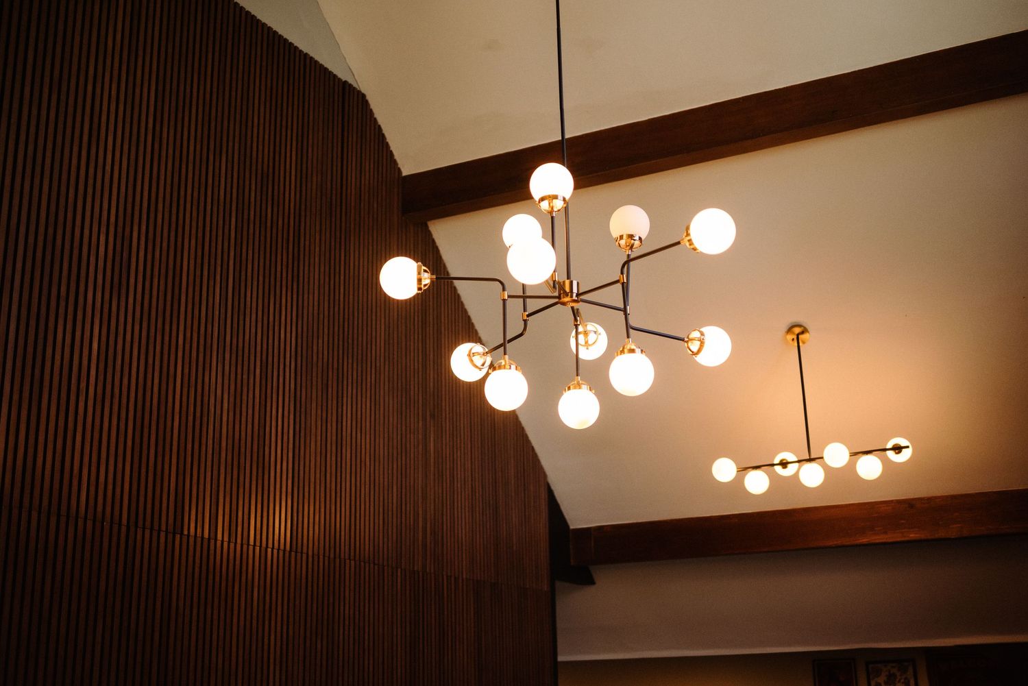 Contemporary pendant lights hang from wooden beamed ceiling in warm ambient lighting.