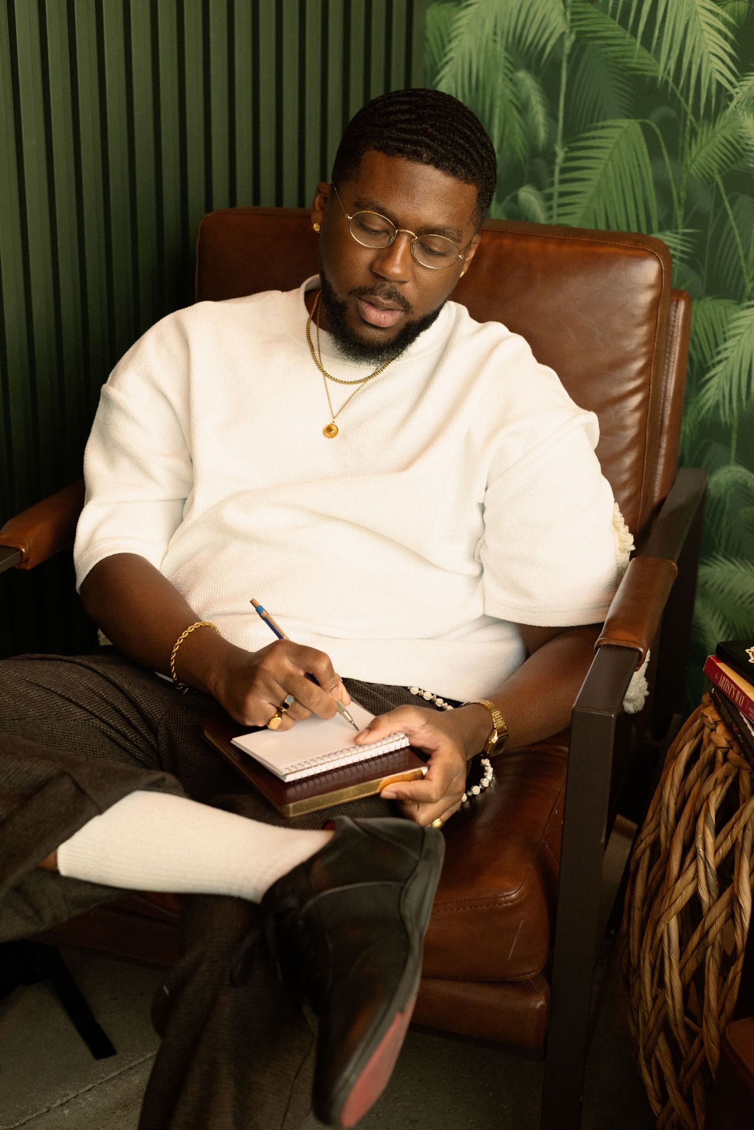 Person wearing glasses and white shirt making notes while relaxing on brown leather couch.