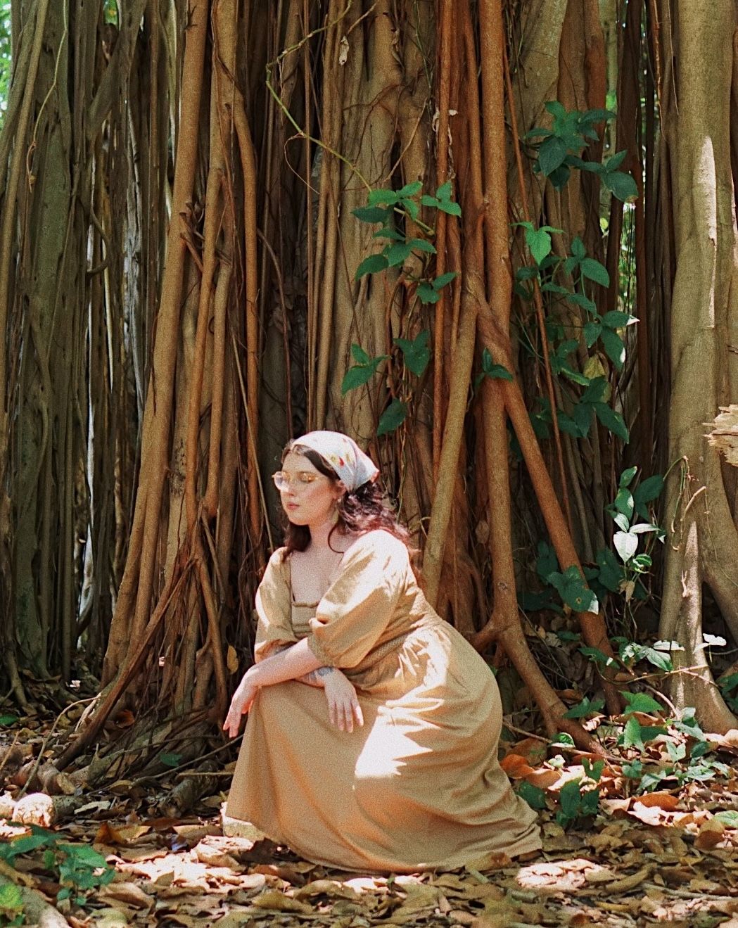 A person in vintage dress sits gracefully against a backdrop of banyan trees with hanging vines.
