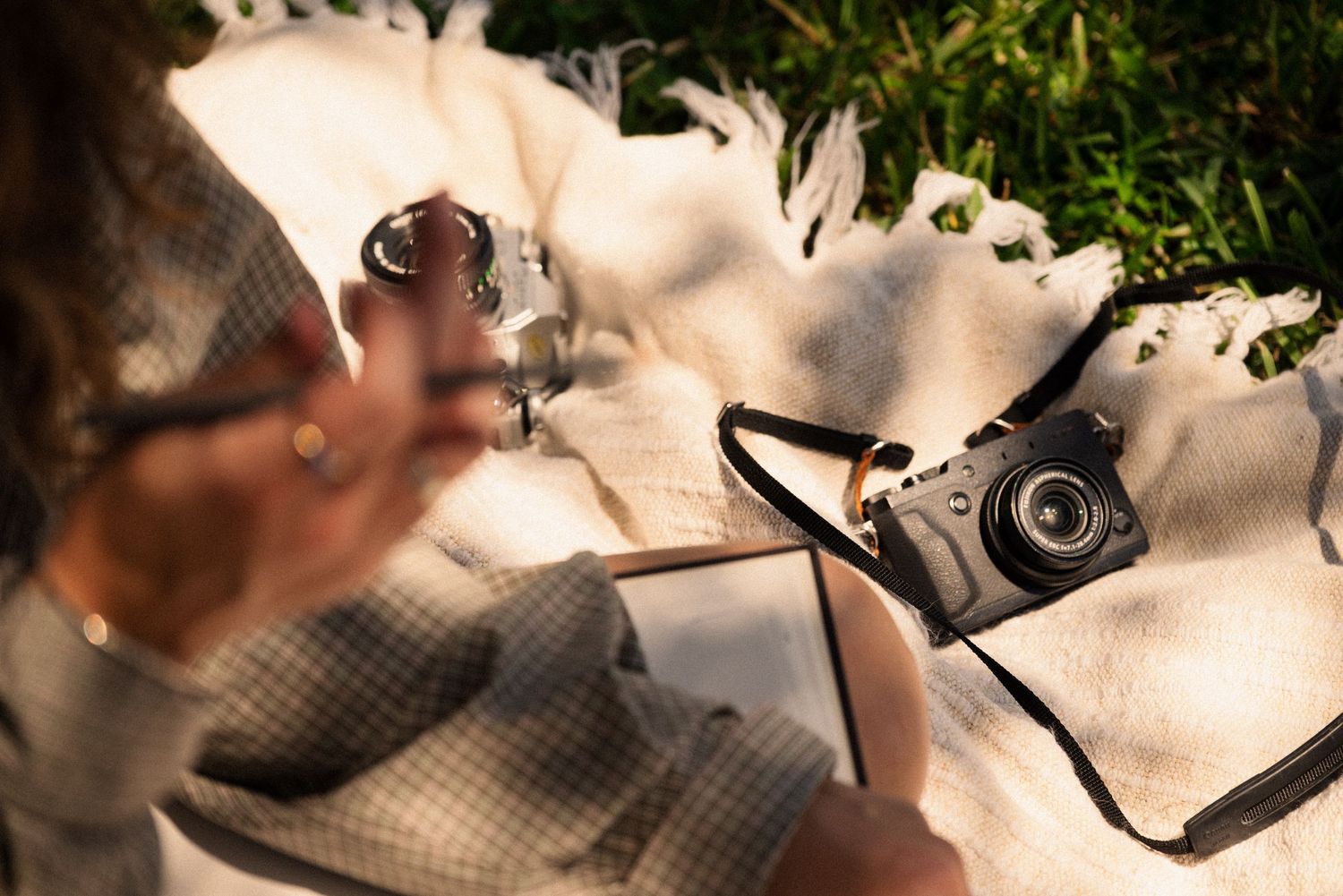 Camera equipment and notebook arranged on a white blanket in dappled sunlight.
