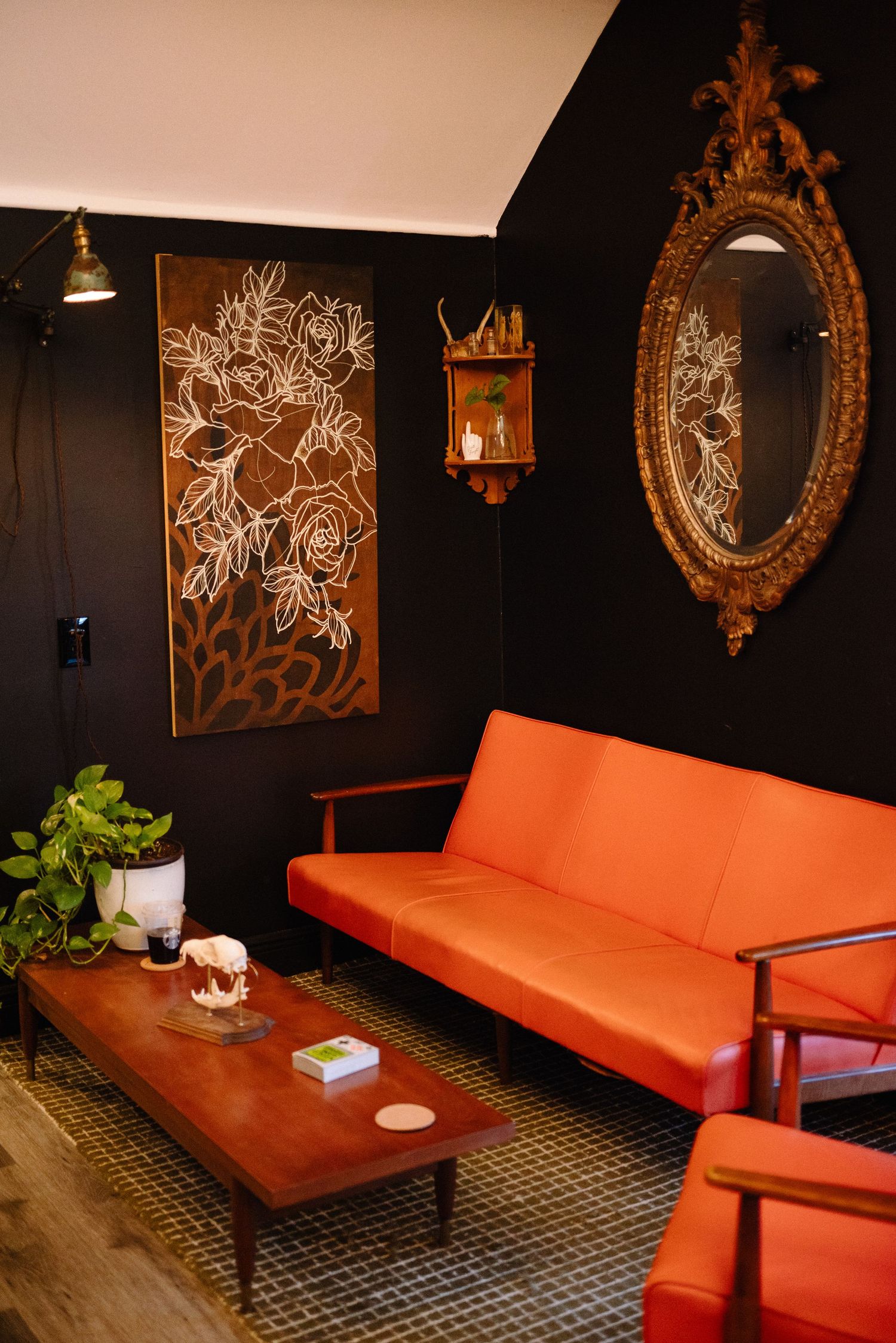 Orange leather couch against black walls with ornate gold mirrors and artistic wall decor.