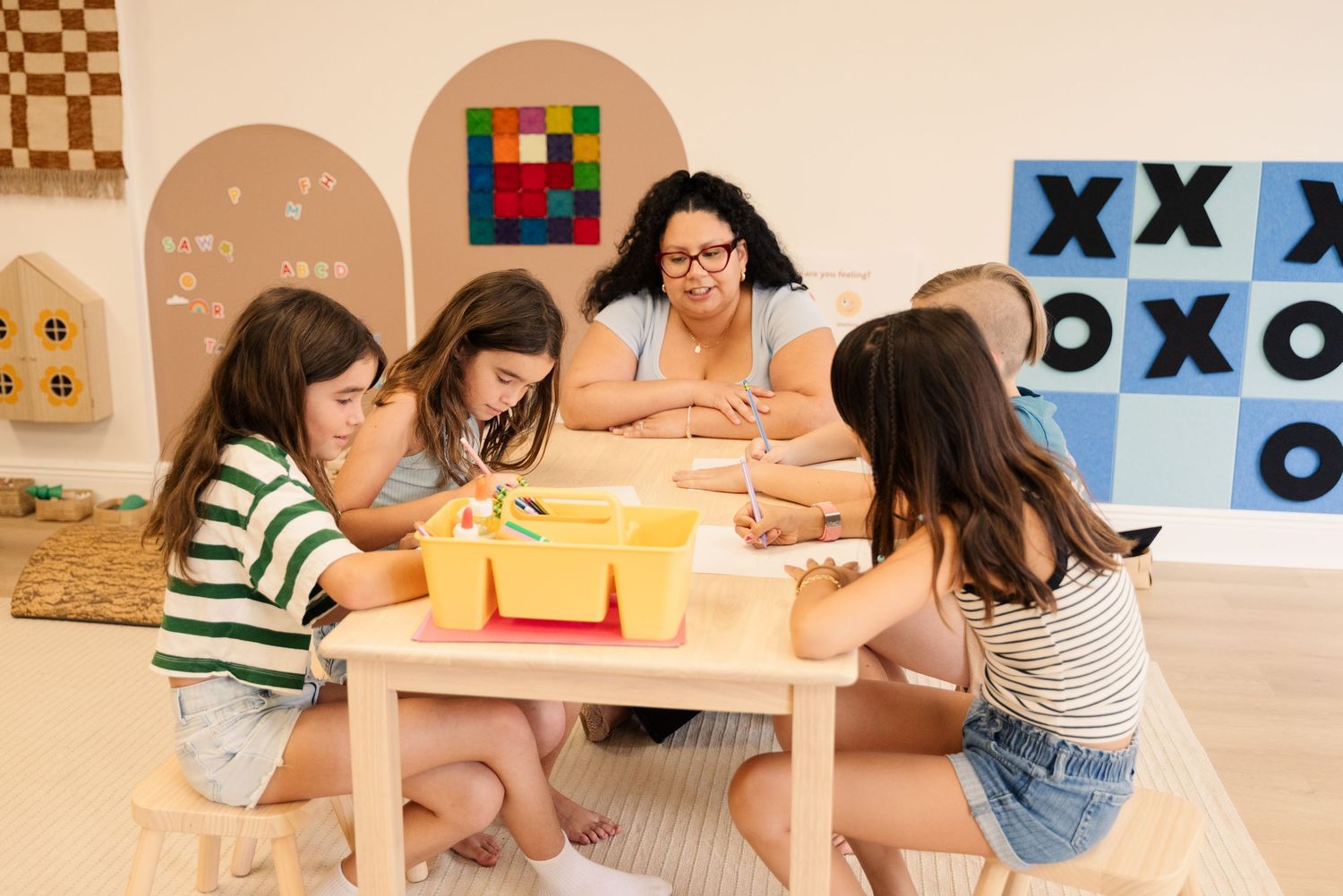 Group gathered around a wooden table for educational activities with colorful game boards in background.