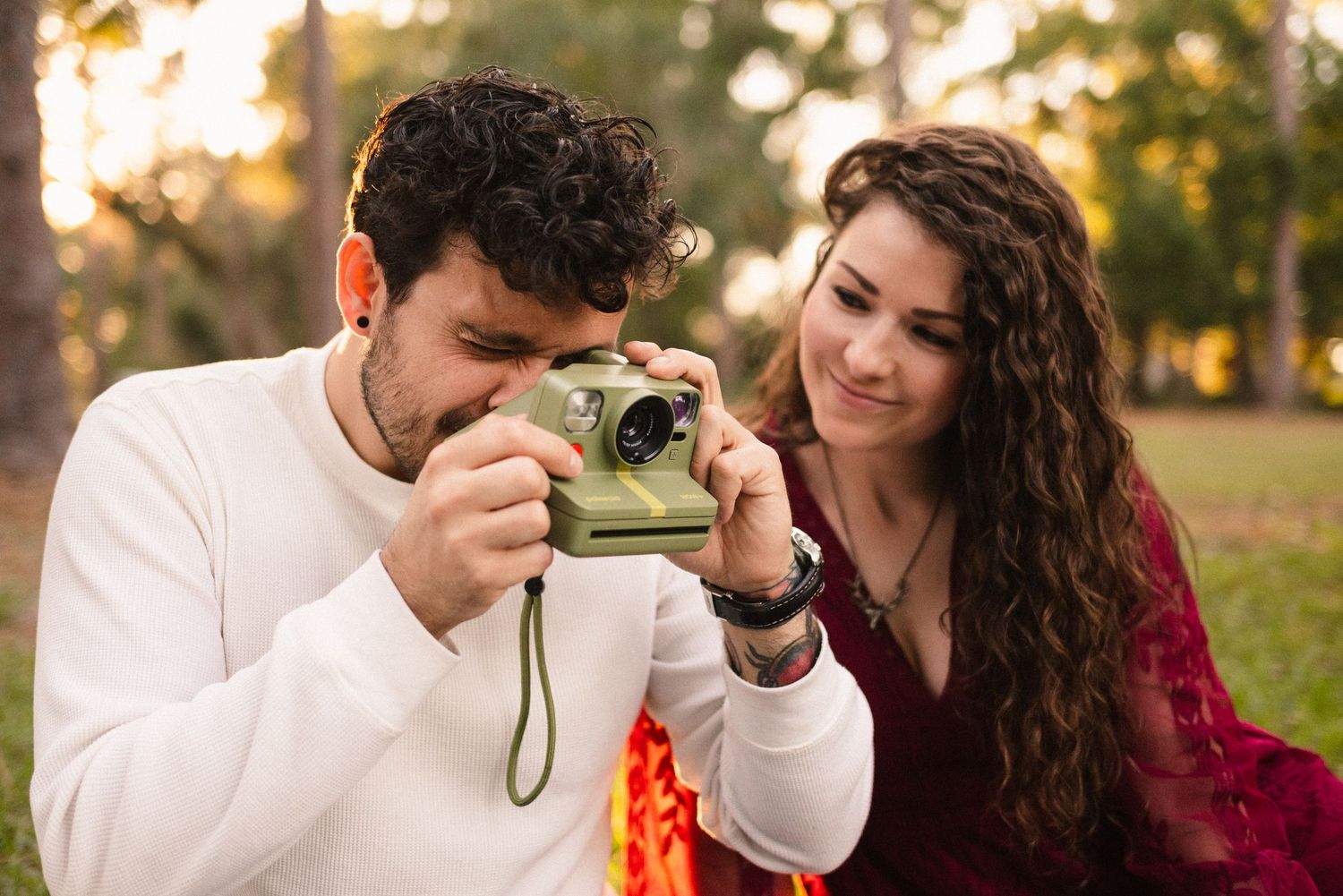 A couple takes photos together with vintage cameras in a park at sunset.