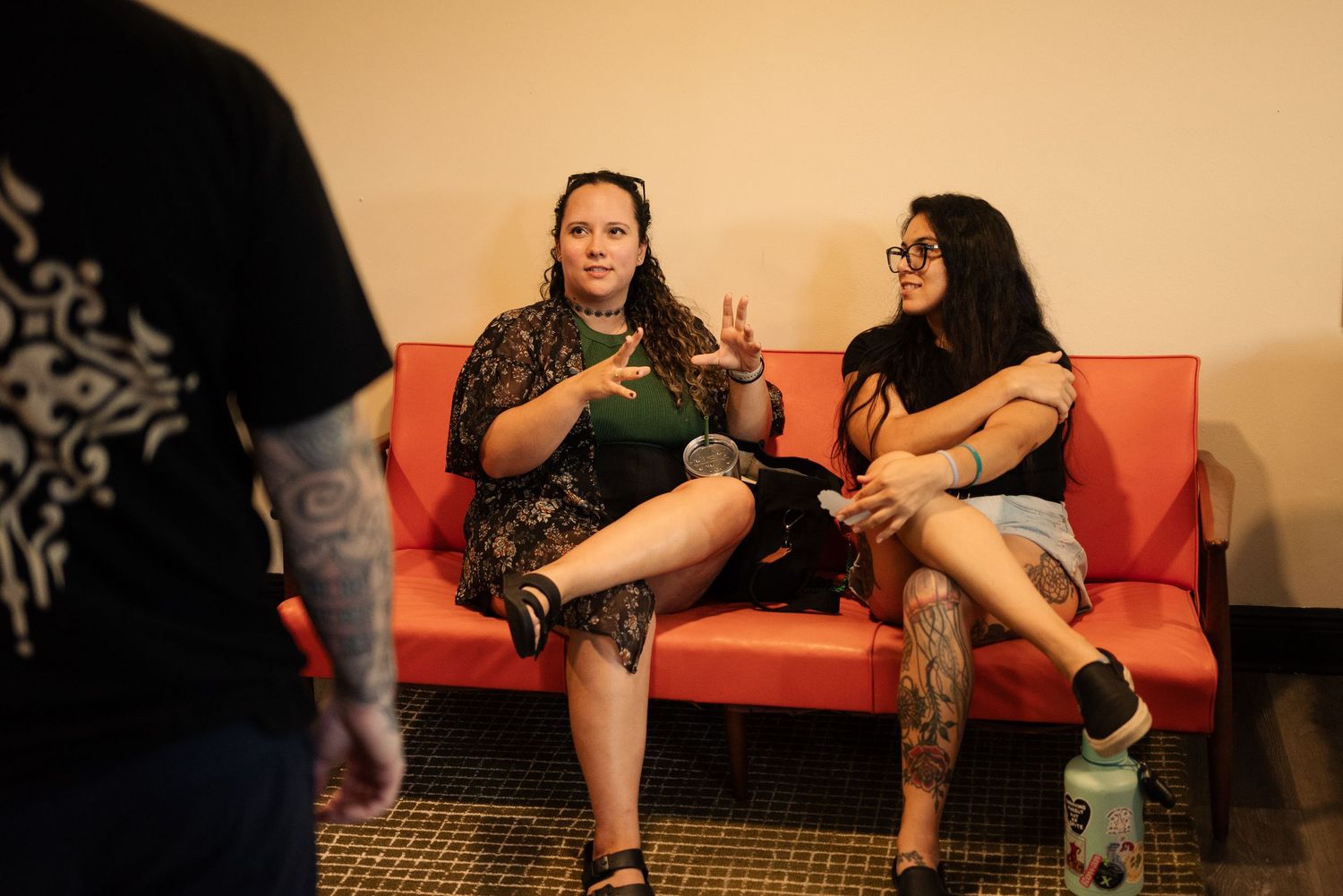 People sitting on an orange couch in a waiting area of a tattoo studio.