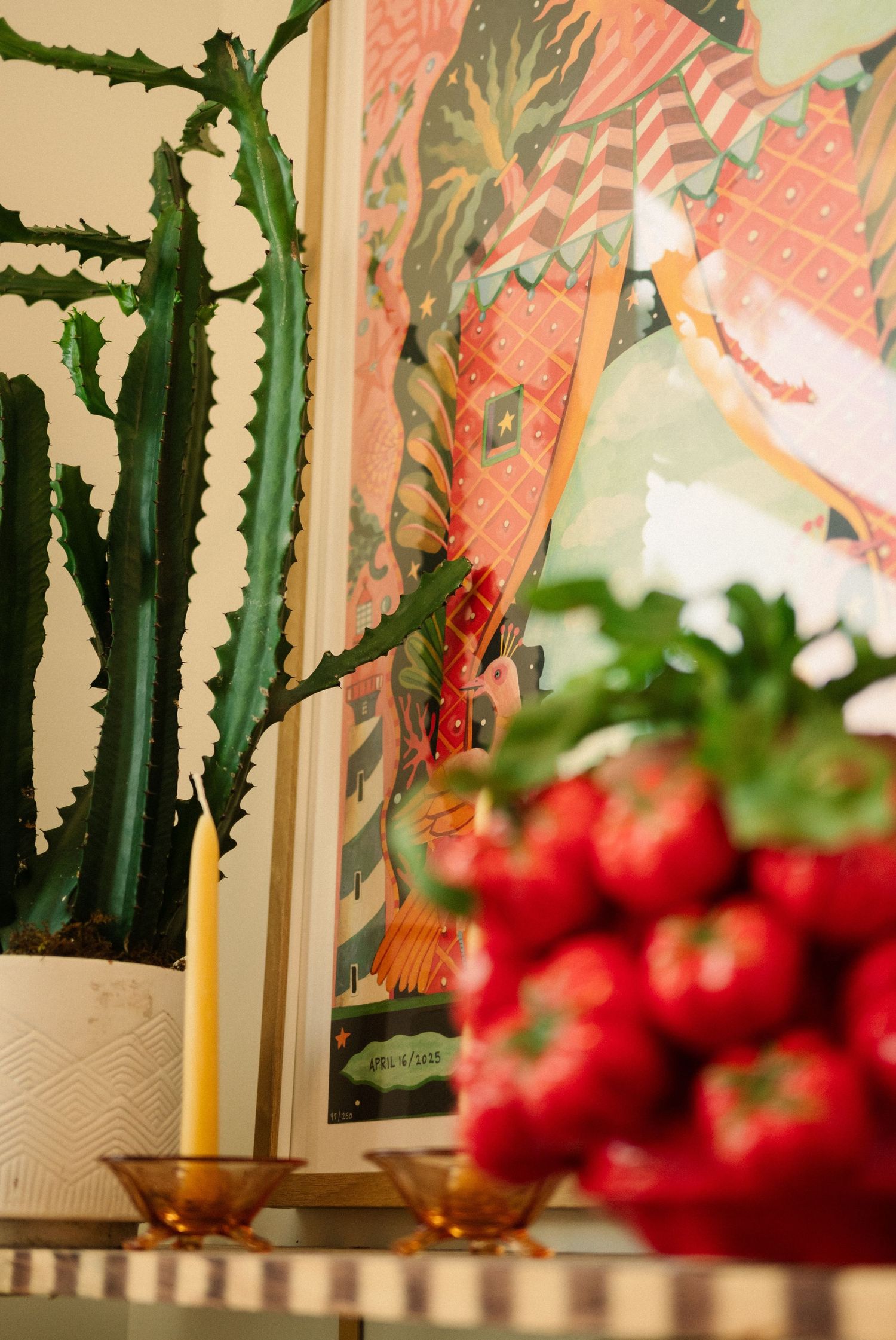 Vibrant red strawberries arranged with tall cactus plants against coral-colored artwork.