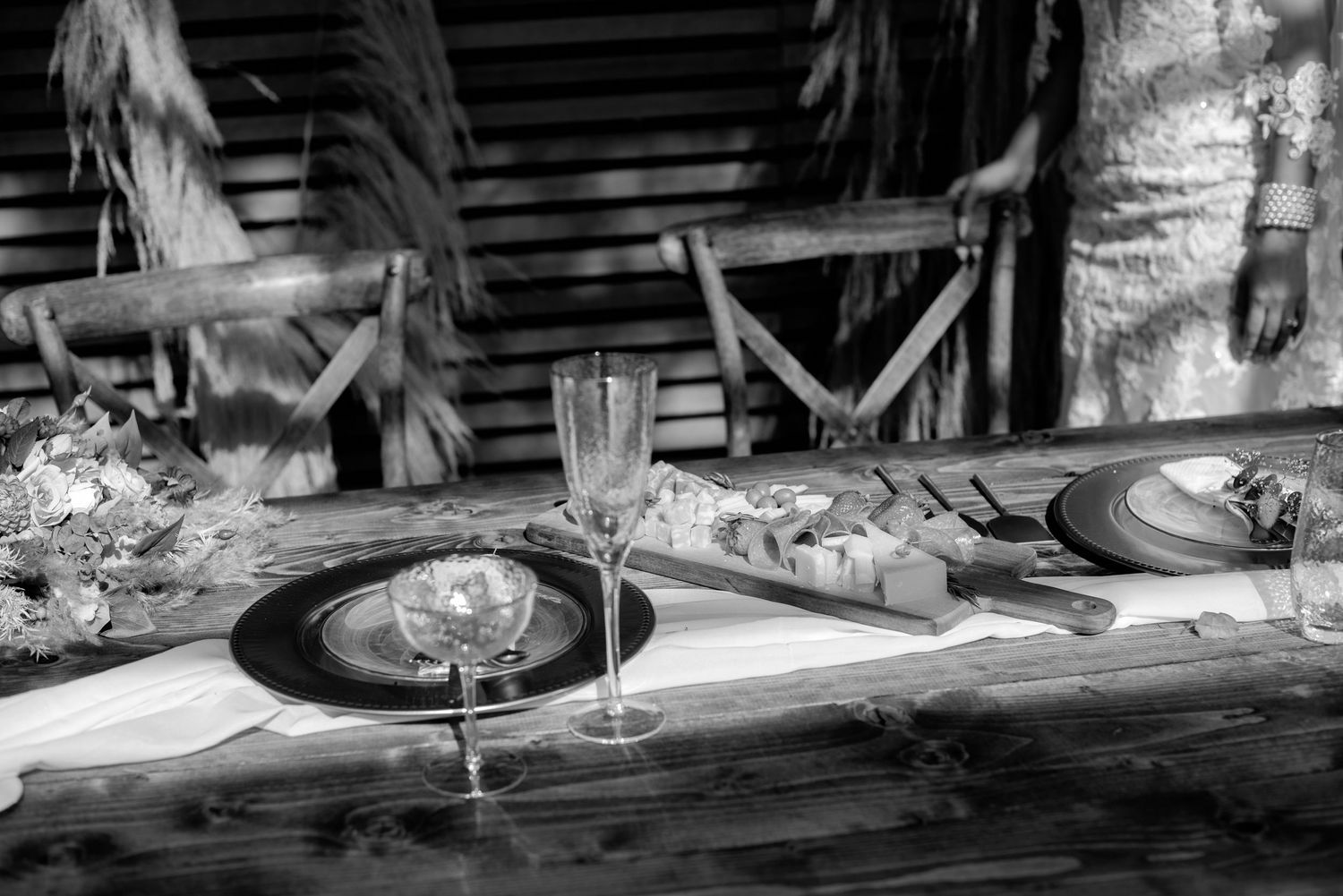 A black and white image of wine glasses and table settings on a rustic wooden surface.