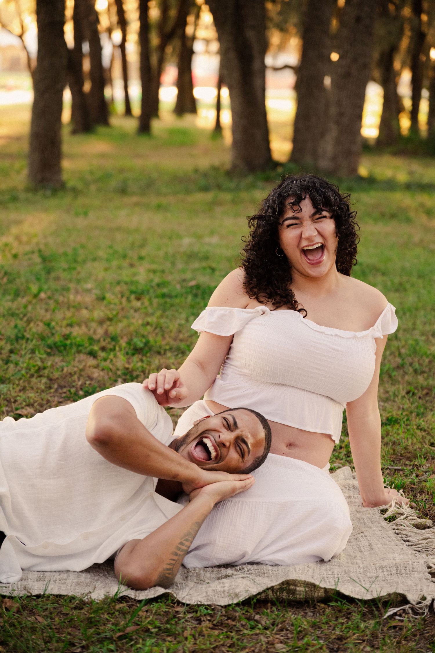 Candid laughter fills the air during a sunset photoshoot on a blanket outdoors.