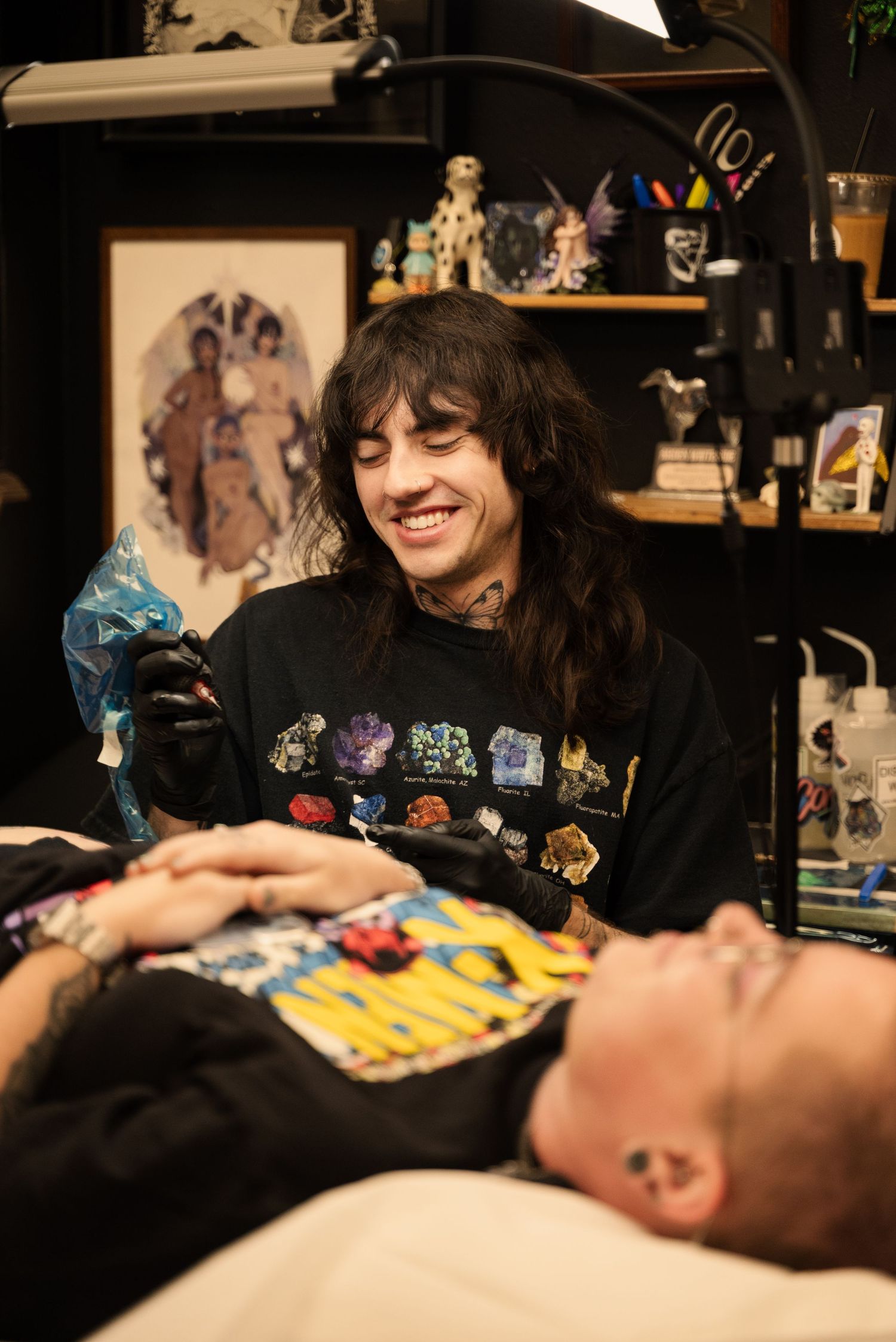Close-up view of a tattoo session in progress with colorful artwork visible in the background.