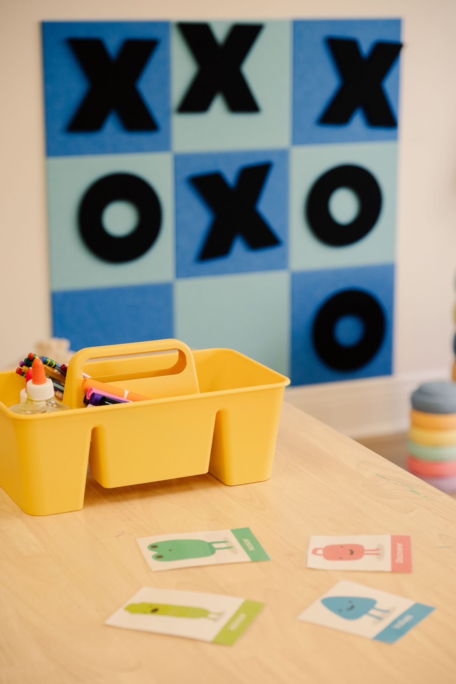 Educational wall display with tic-tac-toe pattern and yellow storage bins on a table.