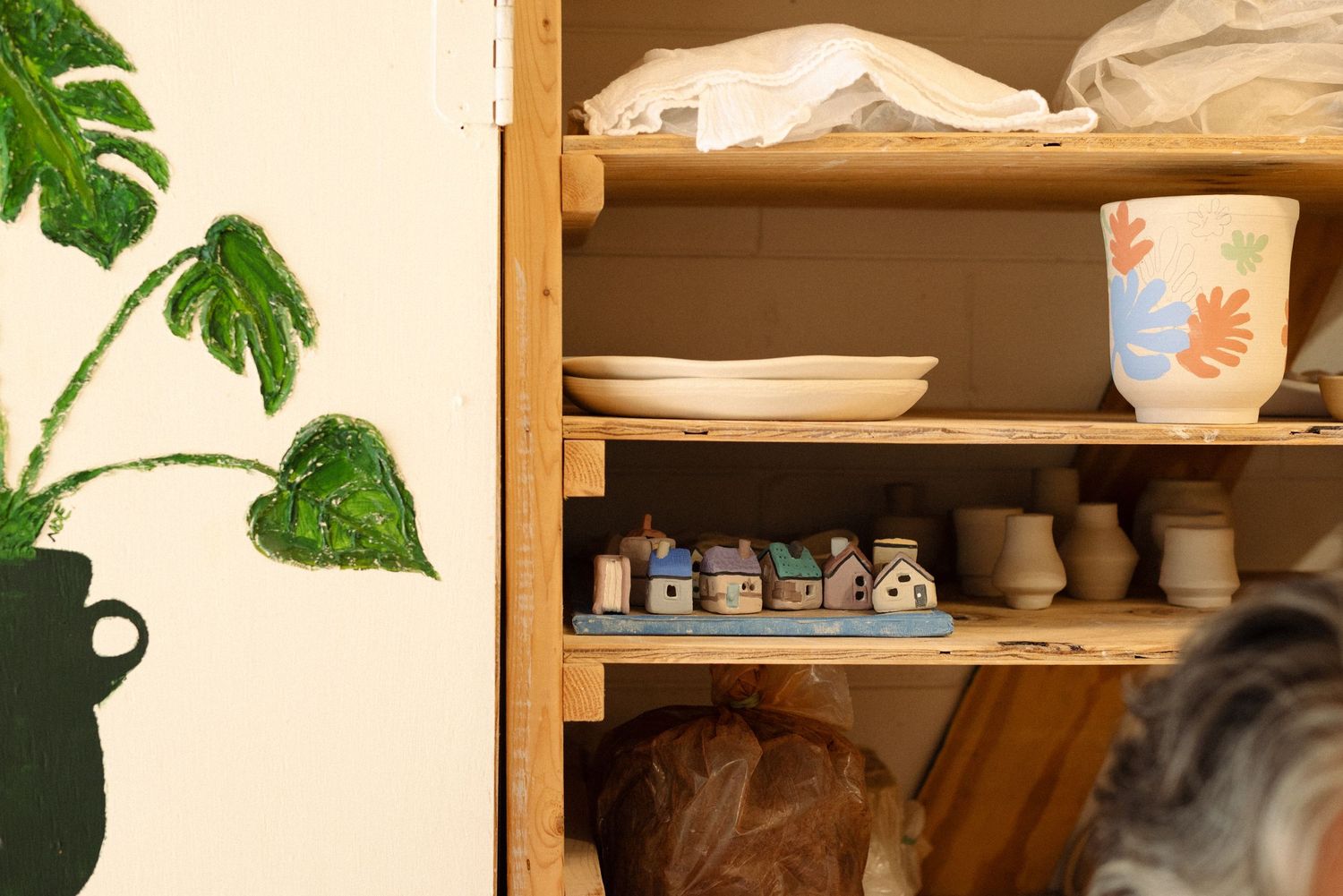 Wooden shelving unit with pottery supplies and tropical leaf decorations.