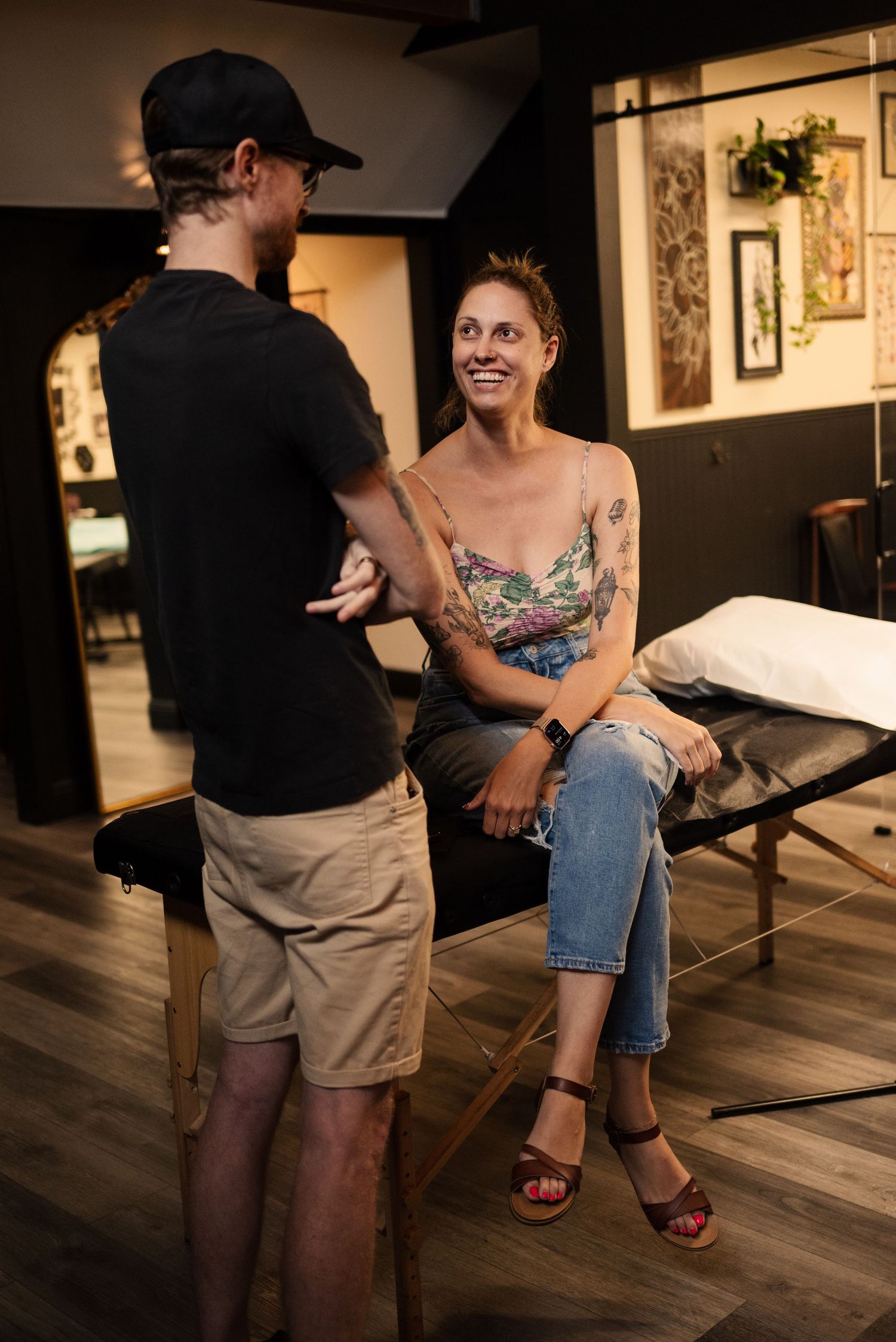 Casual conversation between artist and client in a warmly lit tattoo studio.