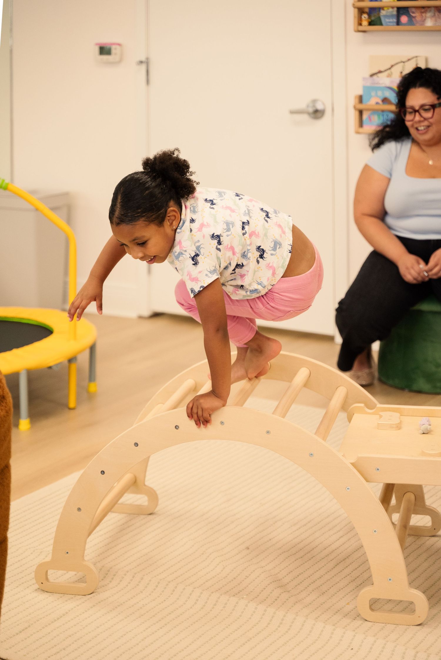 Child climbing on wooden play equipment in an indoor play area.