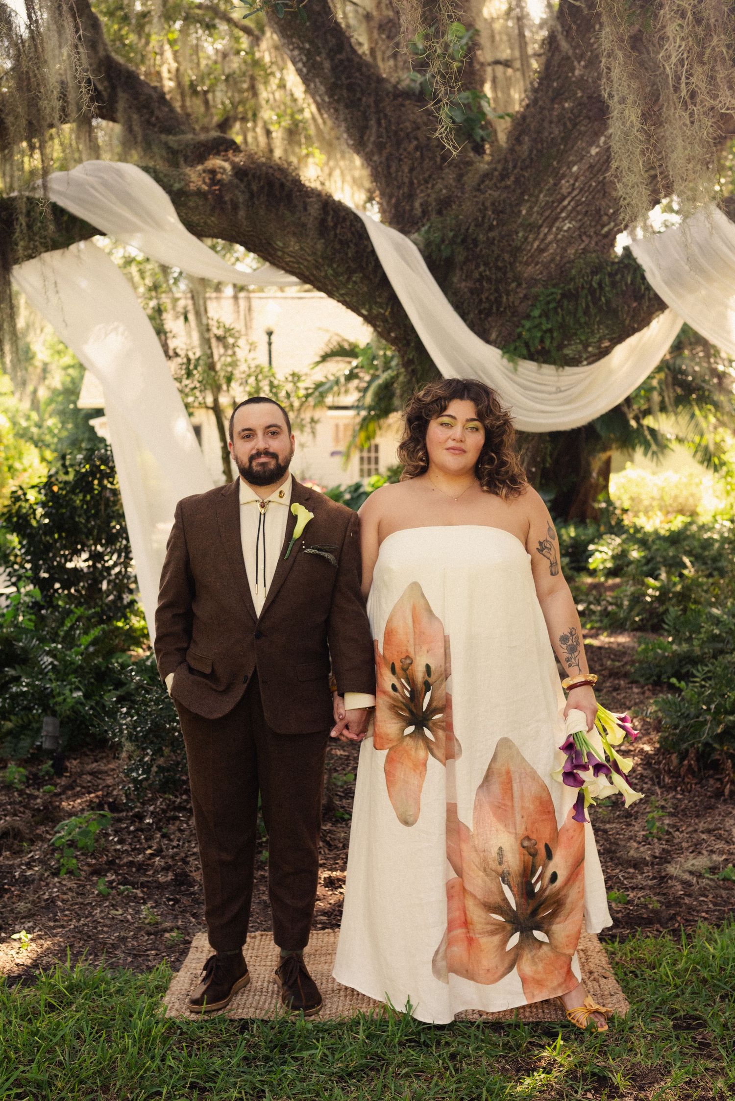 A wedding portrait under draped white fabric with a brown suit and floral dress.