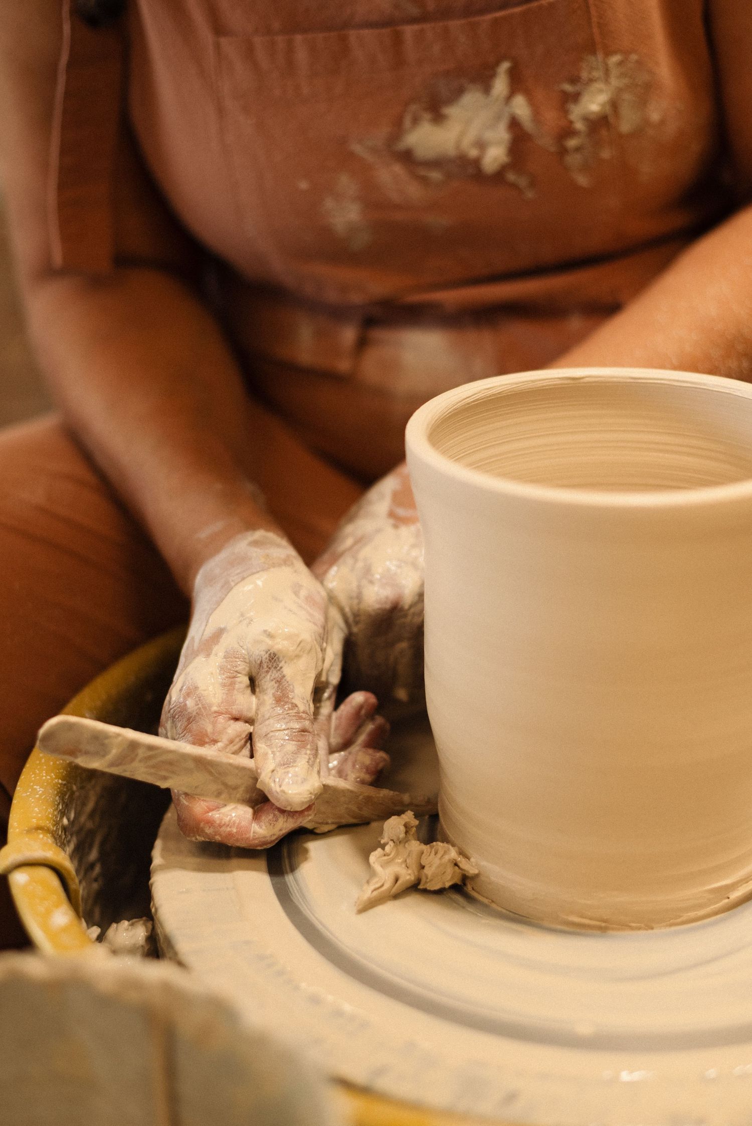 Close-up of ceramic vessels being formed on pottery wheel with clay tools nearby.
