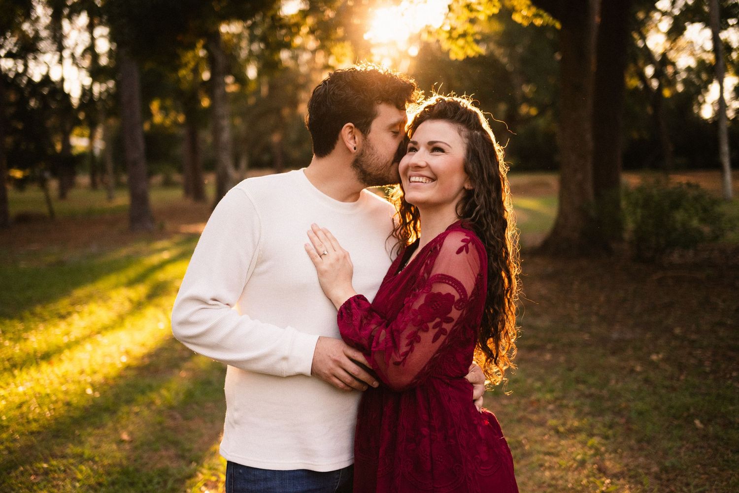 Couple sharing intimate moment in burgundy and white attire during golden hour photoshoot.
