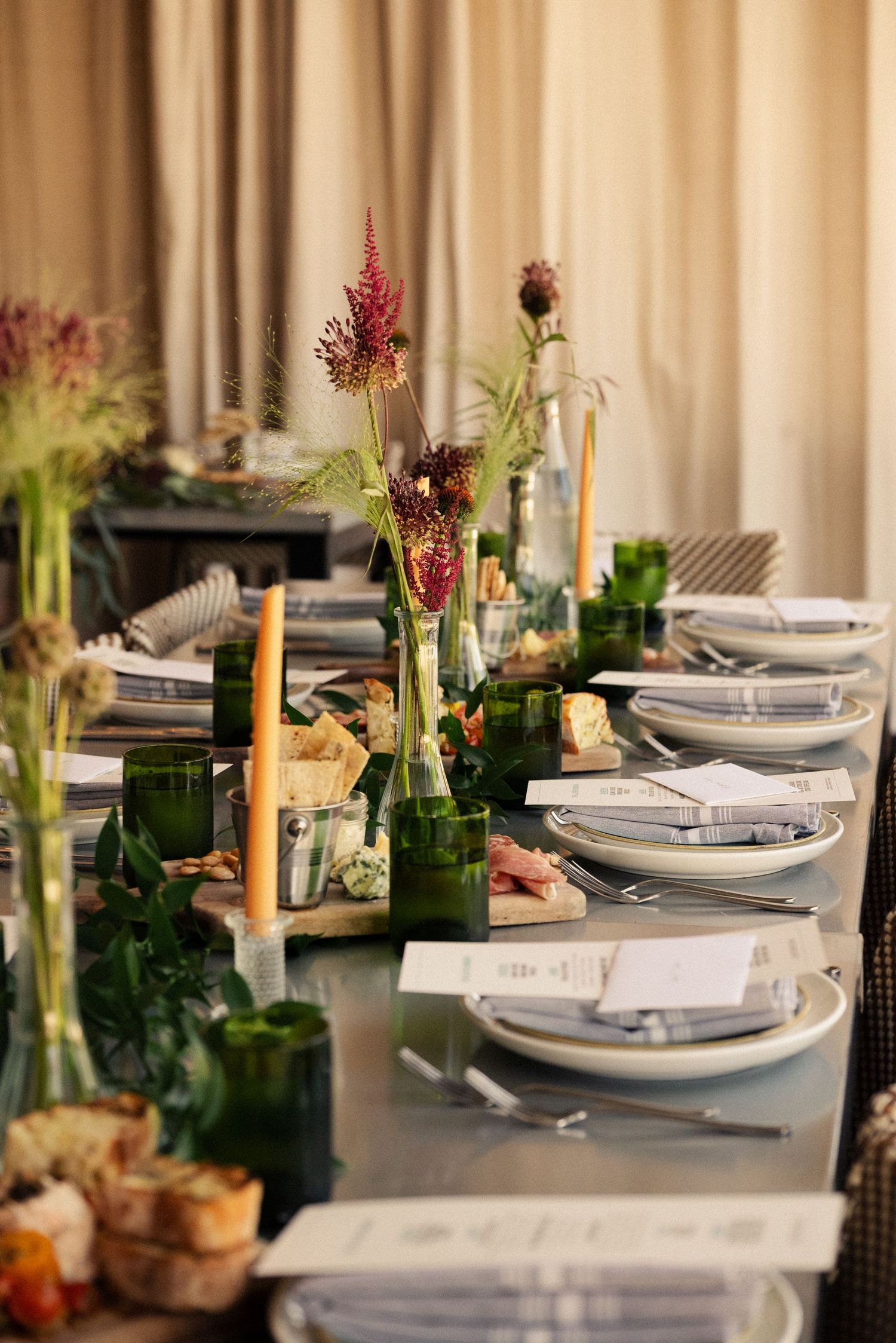 Elegant table setting with green bottles, pink flowers, and white plates for a formal dinner party.