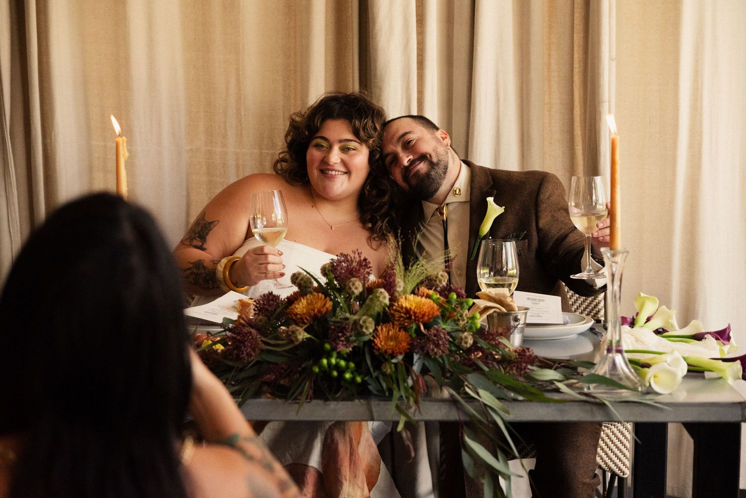 A couple sits at their reception table with candlelight and floral centerpiece.