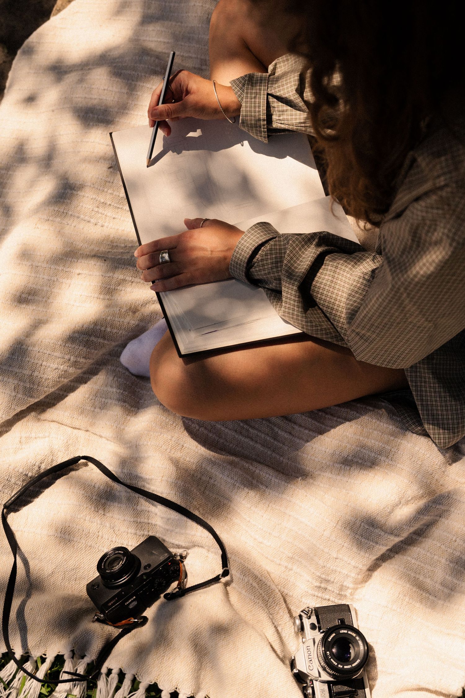 Hands writing in a notebook on a sunlit surface with dappled shadows.