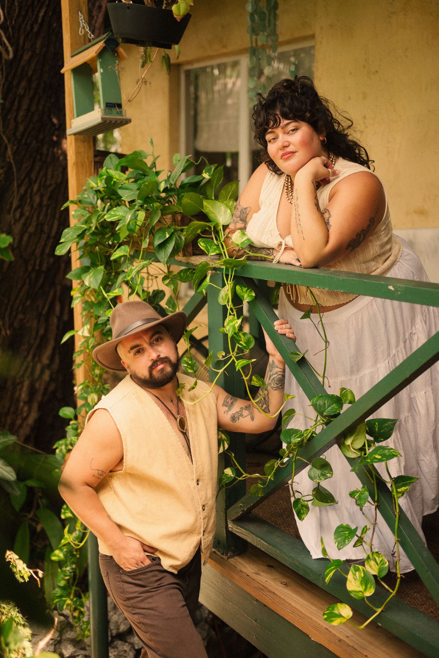 Couple shares tender moments on a green porch railing surrounded by climbing vines.