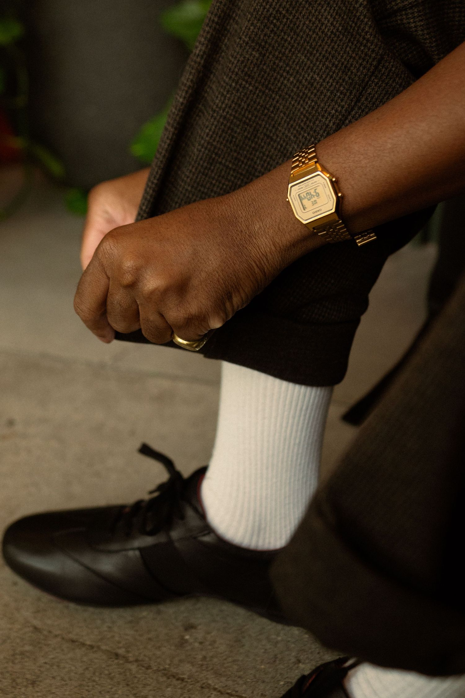 Detail shot of black shoes, white socks, and gold watch against dark background.