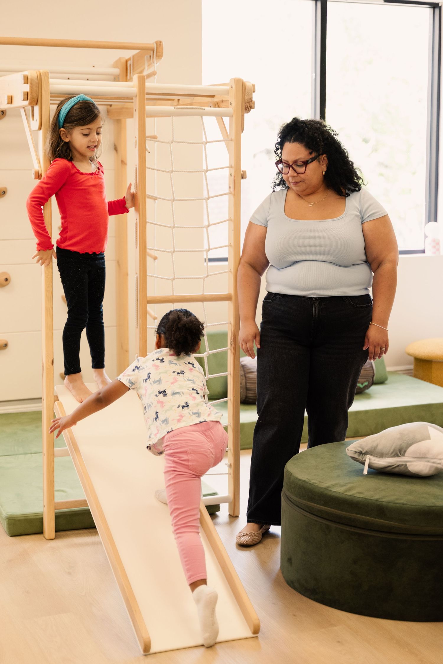 Indoor play area with wooden climbing equipment and exercise mats.