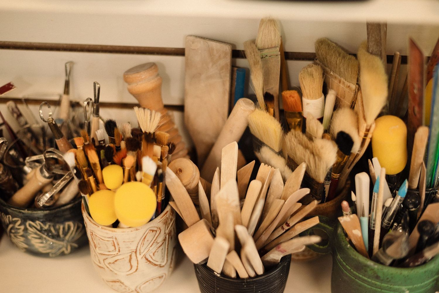 Collection of pottery tools and brushes organized in containers on a shelf.