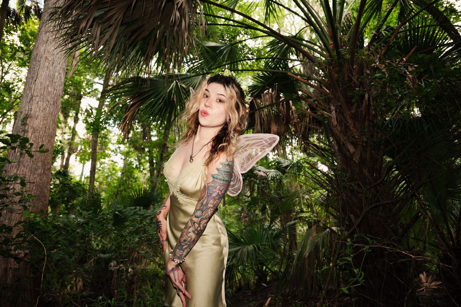 Fairy figure in silk dress poses gracefully among tropical palm trees.