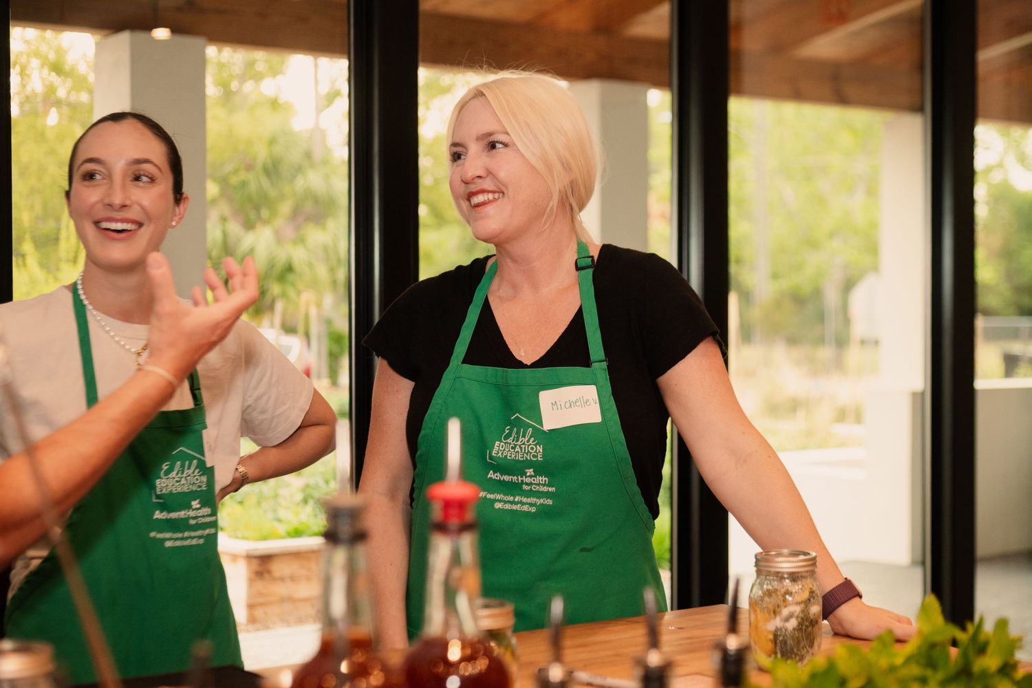 Cooking workshop attendees in green aprons smile while participating in a hands-on culinary demonstration.