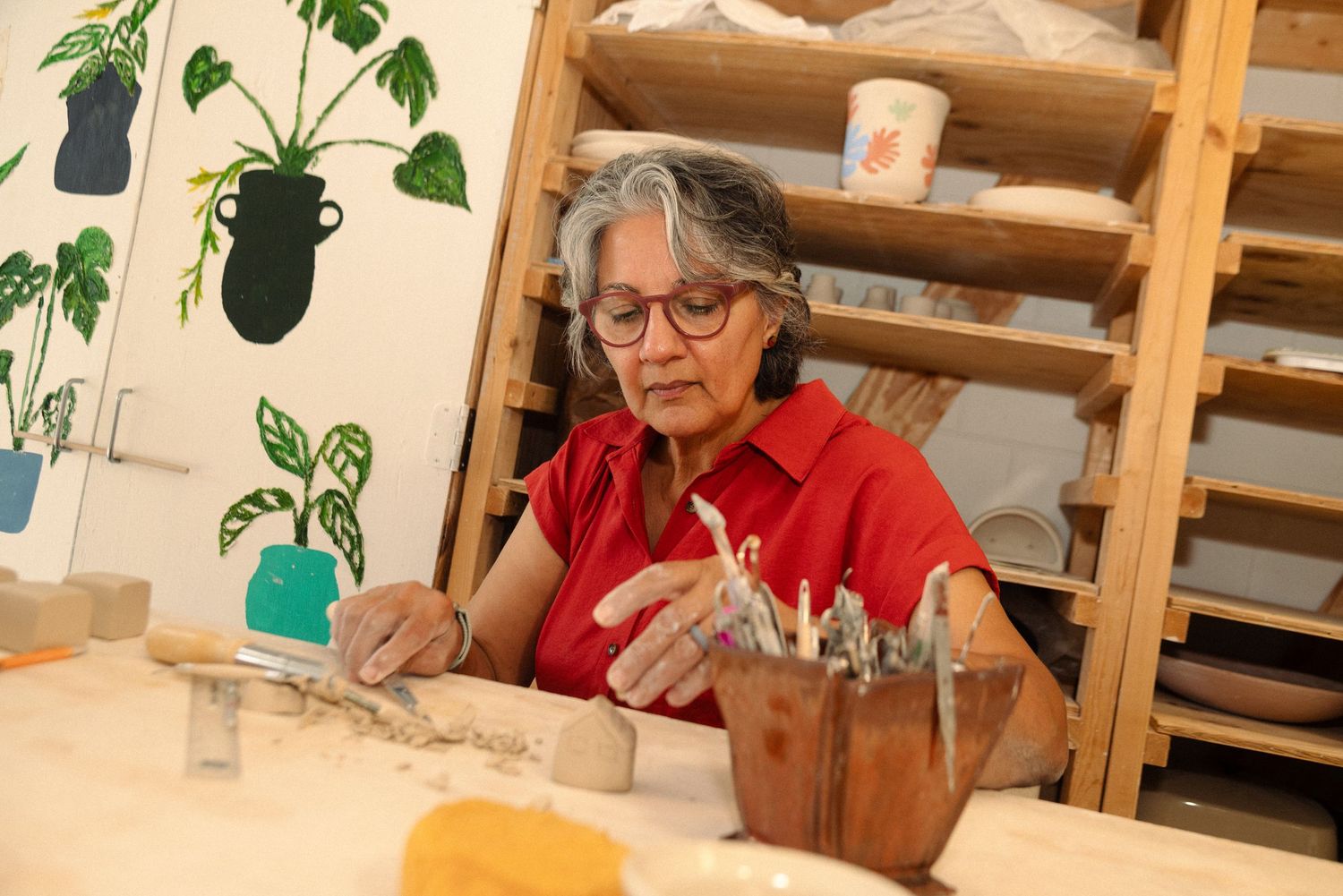 A pottery studio workspace with wooden shelves displaying various ceramics and supplies.