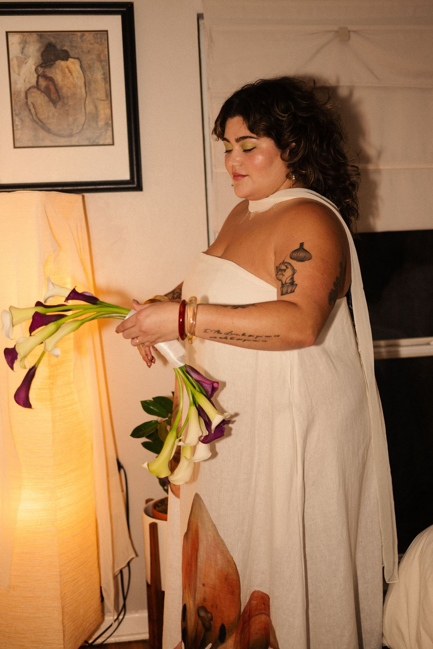 Person in white dress arranges calla lily flowers in warm indoor lighting.