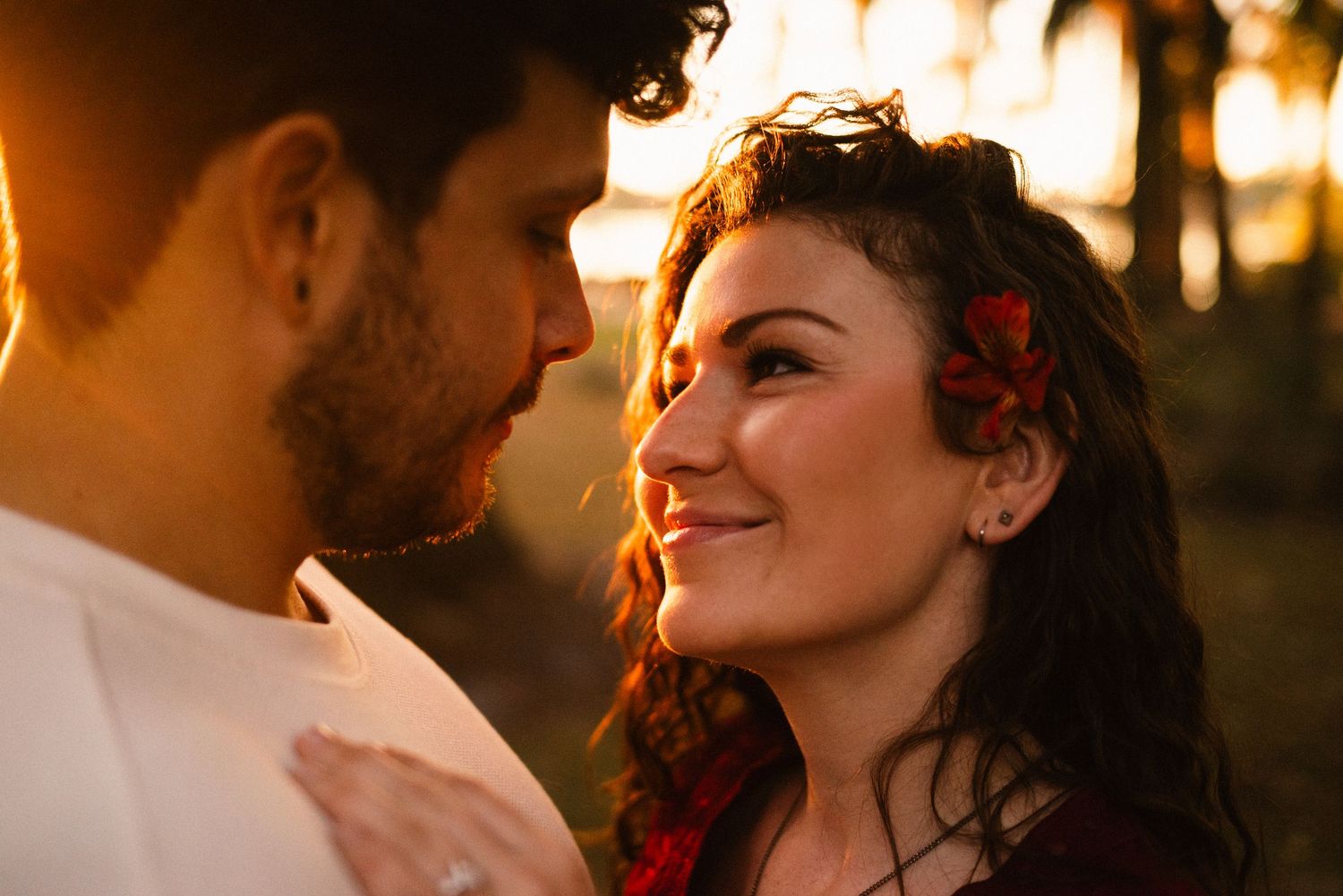 A couple gazes at each other lovingly during golden hour with red floral accents.