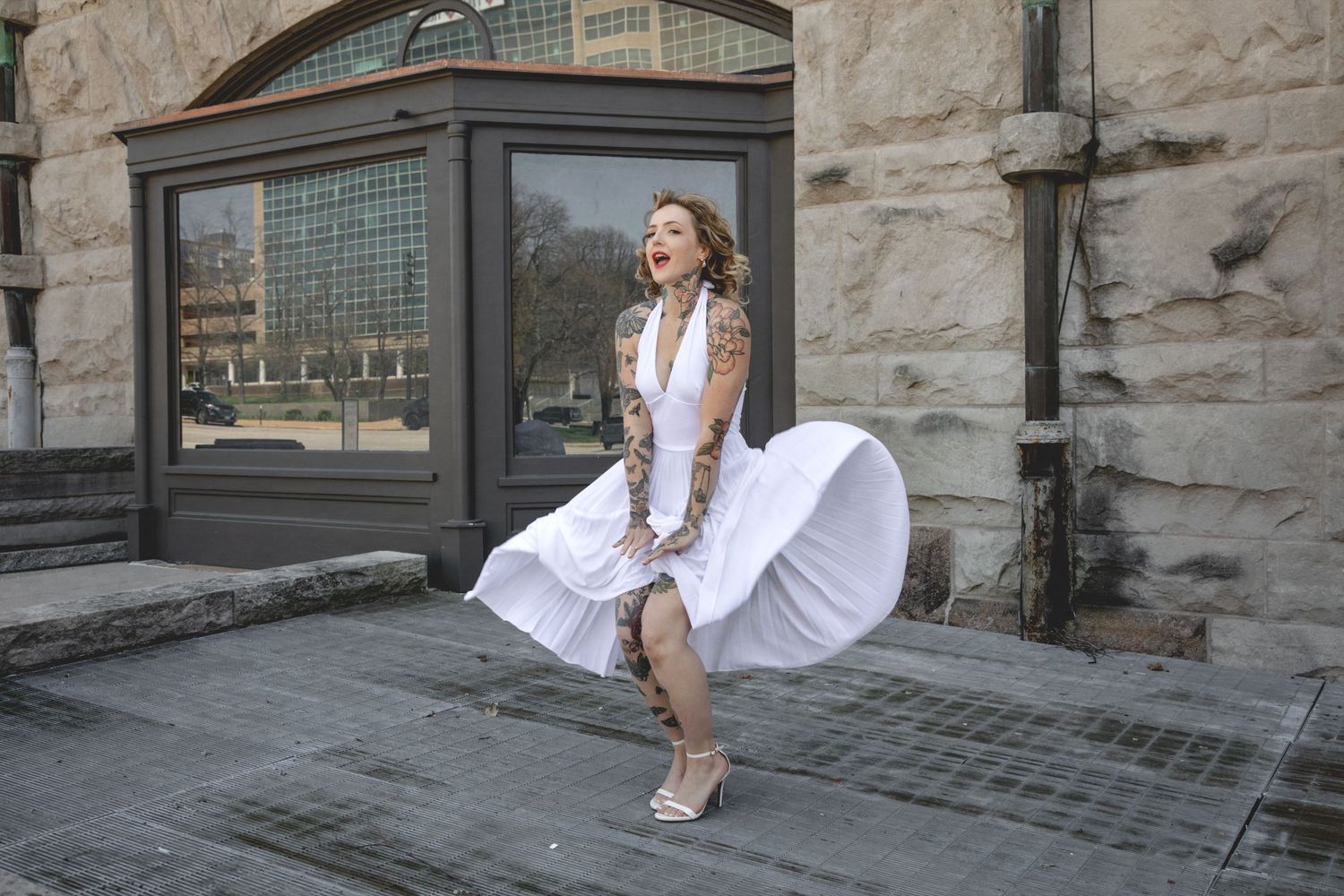 A person in a flowing white dress sits on stone steps against a rustic architectural backdrop.