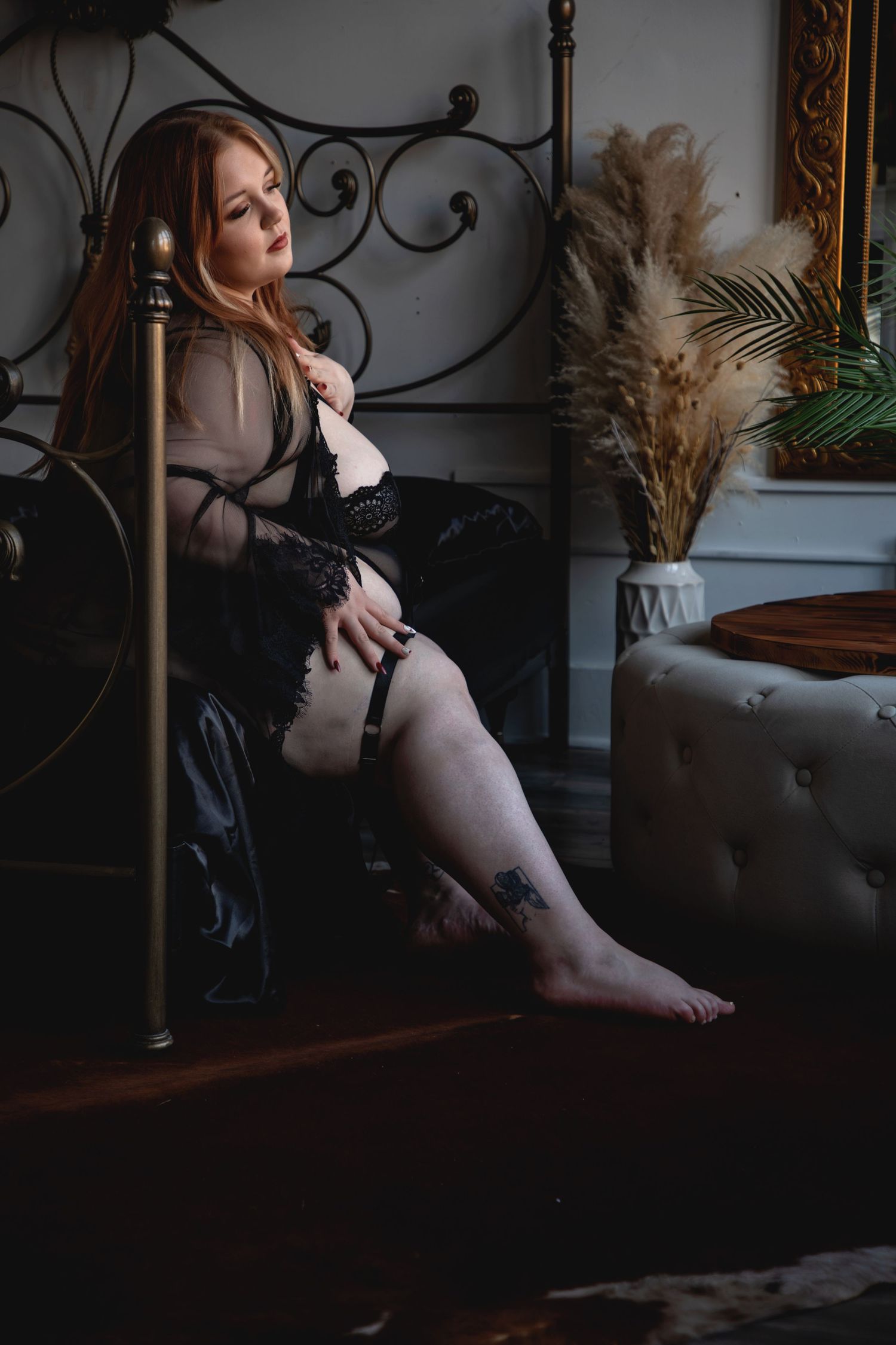 Moody boudoir photo with dark tones featuring lingerie against ornate furniture and pampas grass decor.