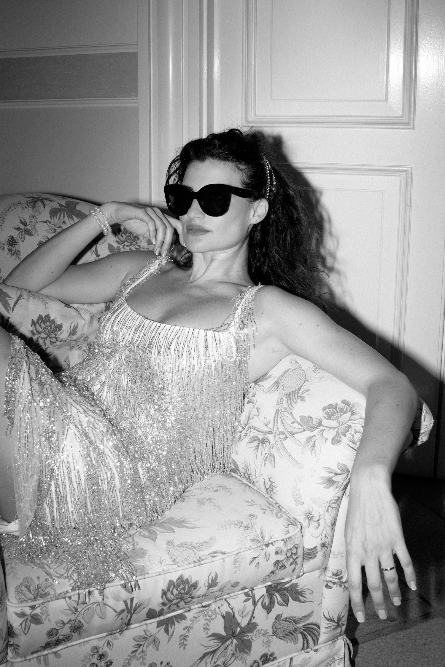 A black and white photo series showing someone reclining on a floral patterned couch wearing sunglasses and a light dress.