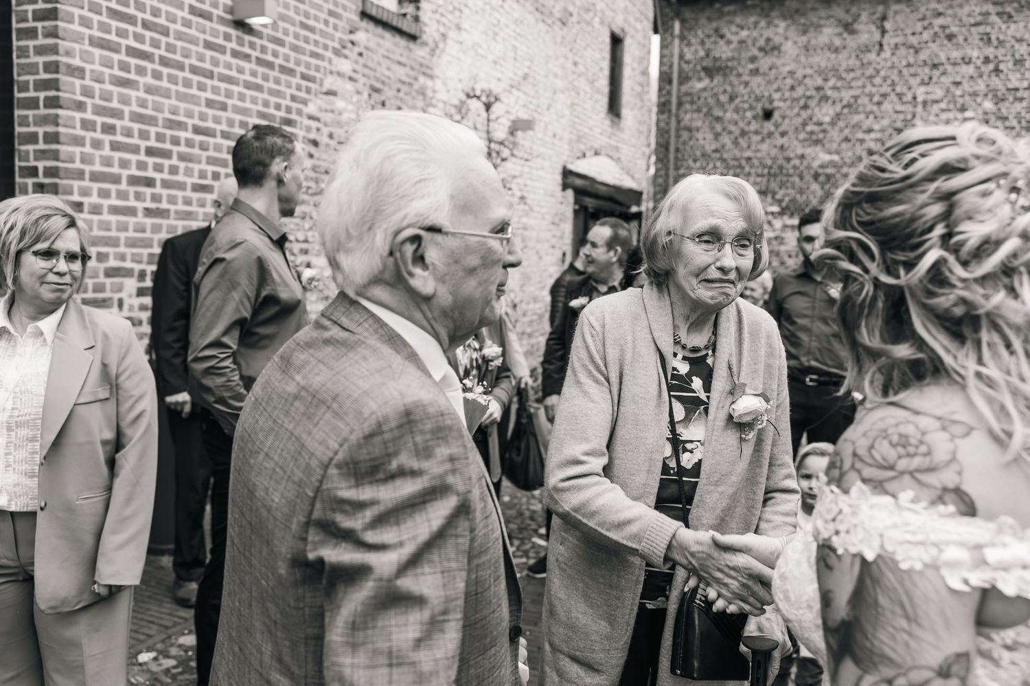 Elderly people gathered outdoors near a brick building for a social event.