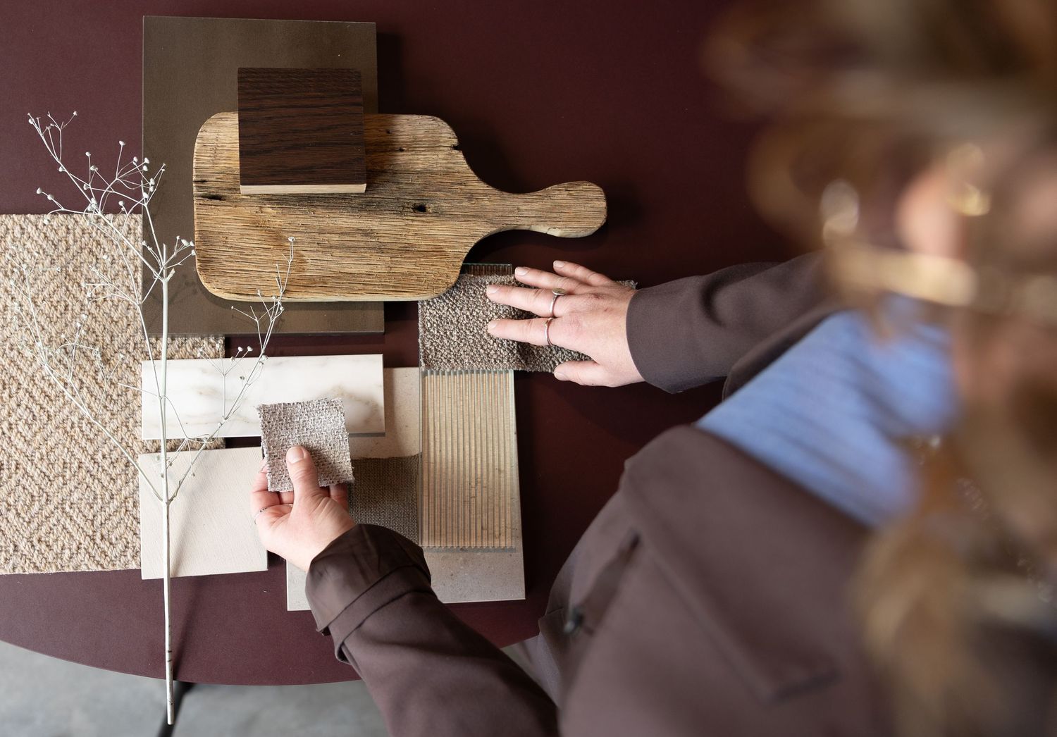 Person arranging wood samples and fabric swatches on a dark red wall for interior design mood board.
